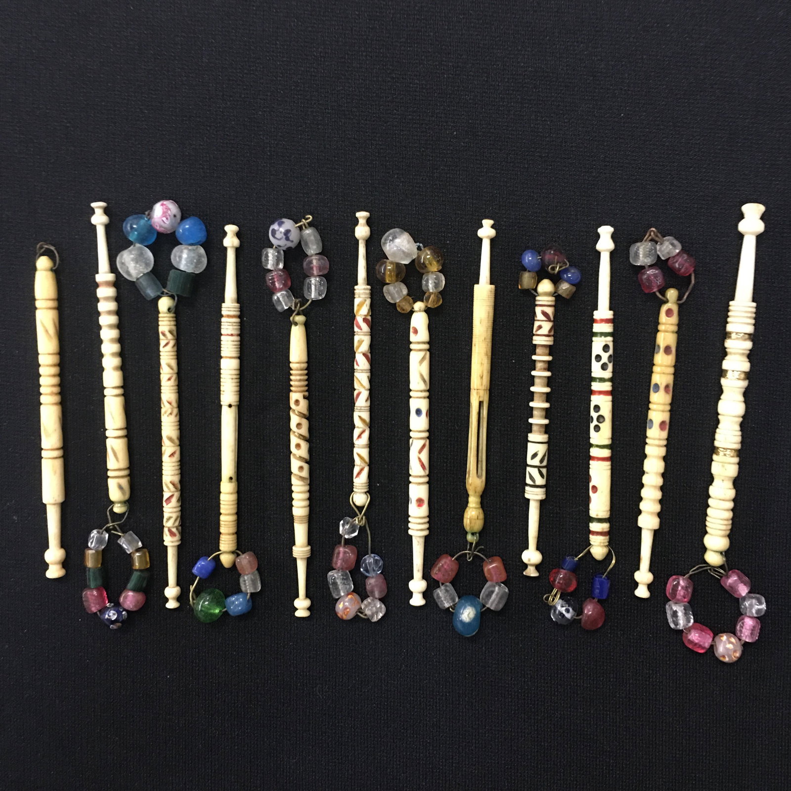 (12) Antique English Bone Midland Lace Bobbins: (12) Antique English Bone Midland Lace Bobbins, all spangled. Designs include colored spots, rings, leaves/vines. One Mother and Babe but missing babe. Two chipped heads. 3.25"-4"