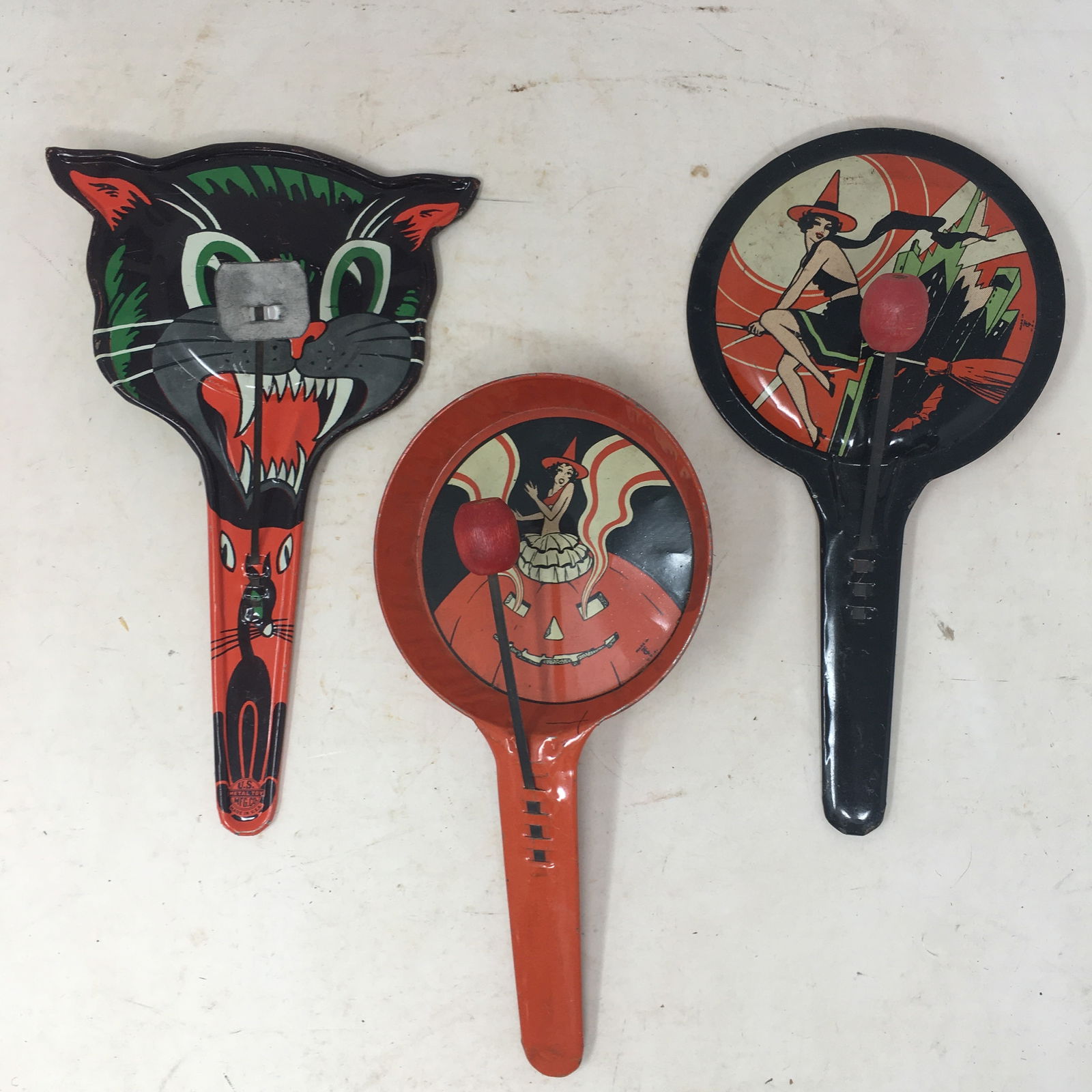 (3) Tin Halloween Noisemakers: (3) Tin Halloween Noisemakers. 1) Witch on broom; 2) Witch & pumpkin, by T Cohn; 3) shape of black cat's head, made by U.S. Metal Toy Mfg. Co. 8"L x 4"W
