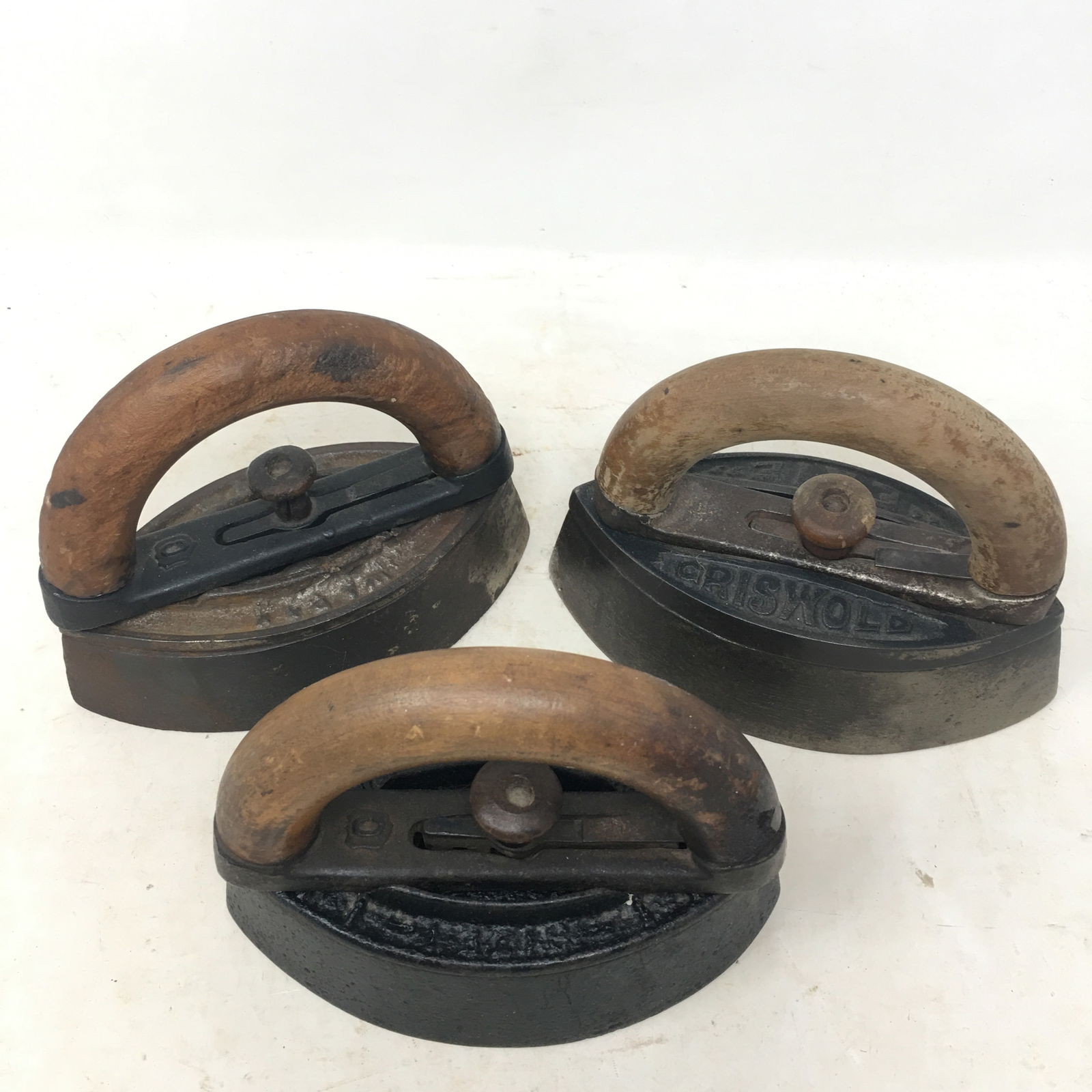 (3) Sad Irons: (3) Sad Irons with detachable wood handles. (1) Griswold Erie, (1) "Wapak, (1) "Size No 50". Largest 7"L x 3.5"W x 5"H