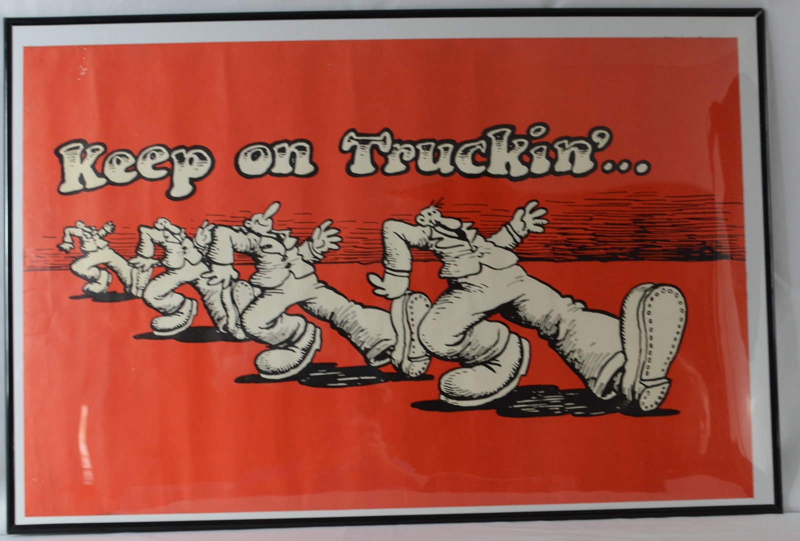 "Keep on Truckin'" Framed Counterculture Poster: Framed "Keep on Truckin'" poster featuring the iconic cartoon walking figures associated with 1960s1970s counterculture pop art imagery. Printed in black and white against a bold red background with