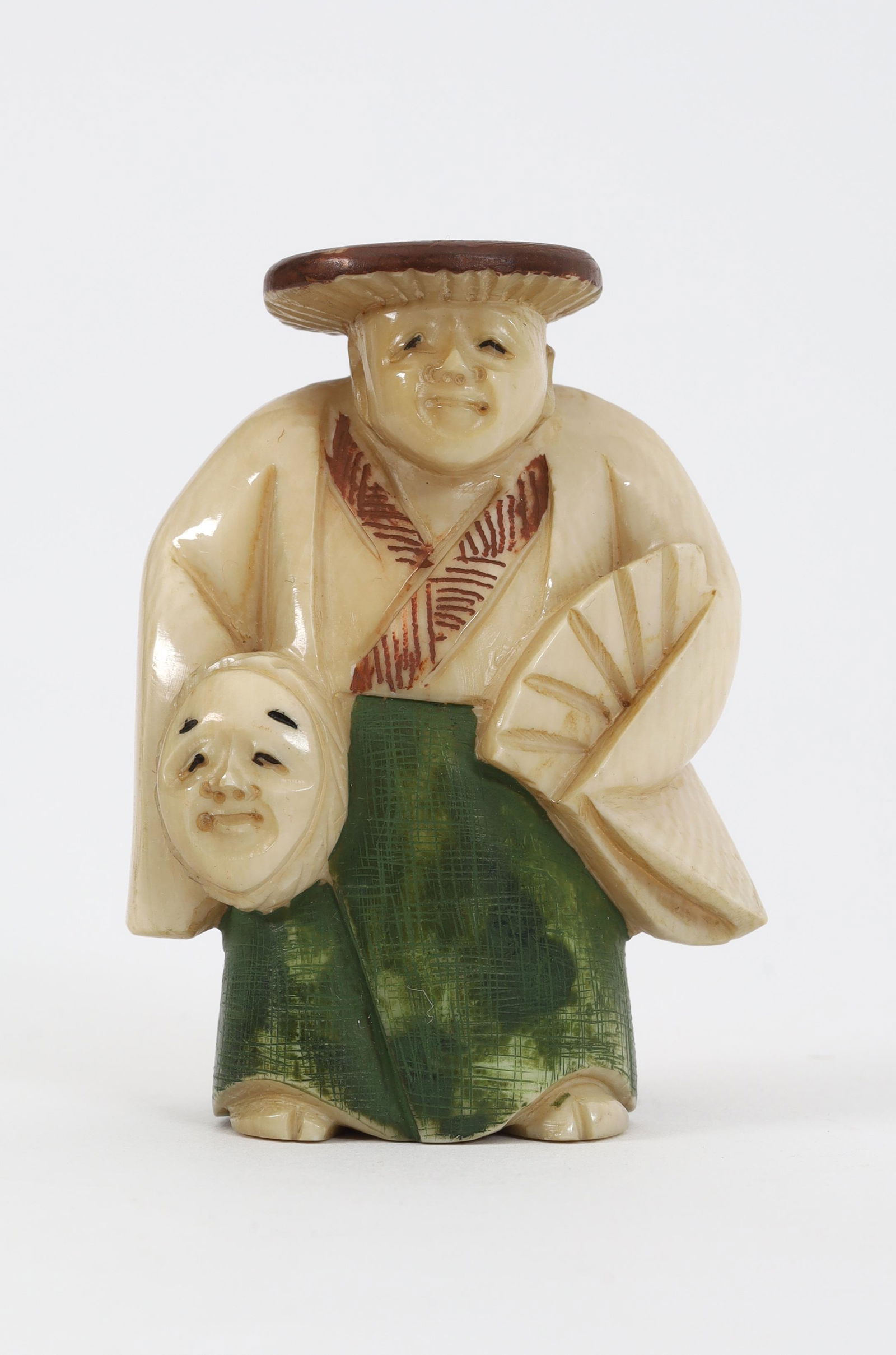 Japanese Netsuke Heian Man Holding Mask Fan Signed: Japanese hand carved netsuke of a man wearing a kasa flat woven straw hat and kimono in the heian style, and holding a mask in one hand and a fan in the other, with hand painted details, signed. 2 inc