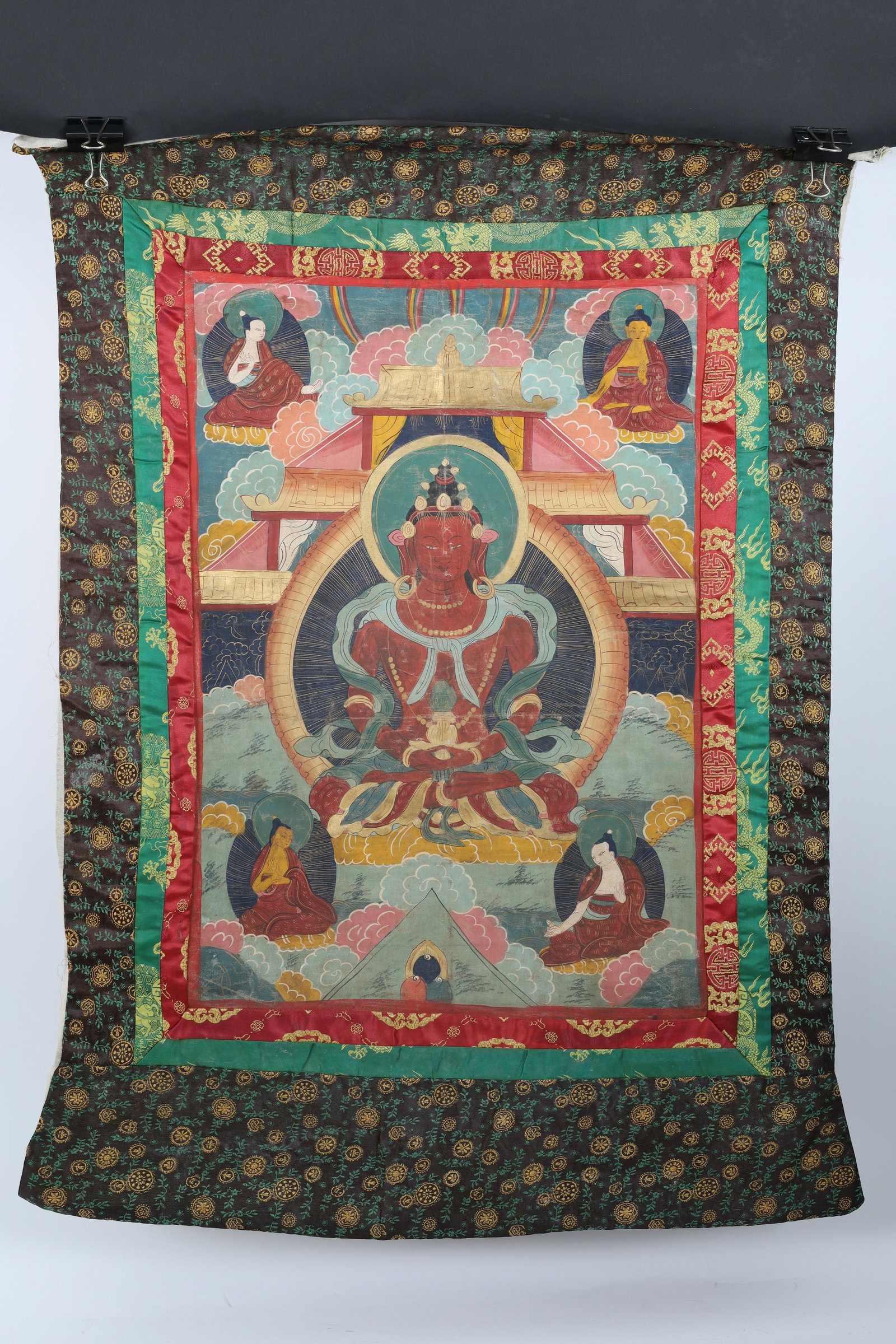 Tibetan Antique Thangka Painted Buddha in Temple: Antique Tibetan thangka with hand painted detailed design with gold highlights showing Buddha in the center within a temple and other deities in the four corners, with hand sewn silk border; this than