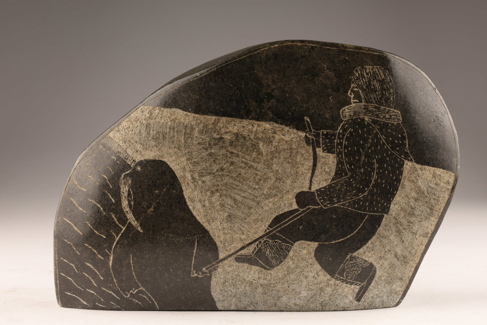 1983 Signed Syllabics Inuit Soapstone Engraving: 1983 Signed Syllabics Inuit Soapstone Engraving depicting a hunter and seal, double sided. Signed on base. 5.5 x 8 x 2.5 inches deep.