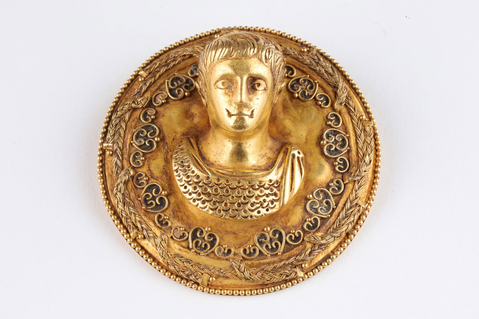 22K Gold Greco-Roman Medallion Shield Portrait: 22K Gold Greco-Roman Medallion High Relief Shield Portrait of a Man, possibly an Emperor. 2 inches diameter x 1 H. Total weight, 58.1 grams. With head formed in the round, decorated with braided swags