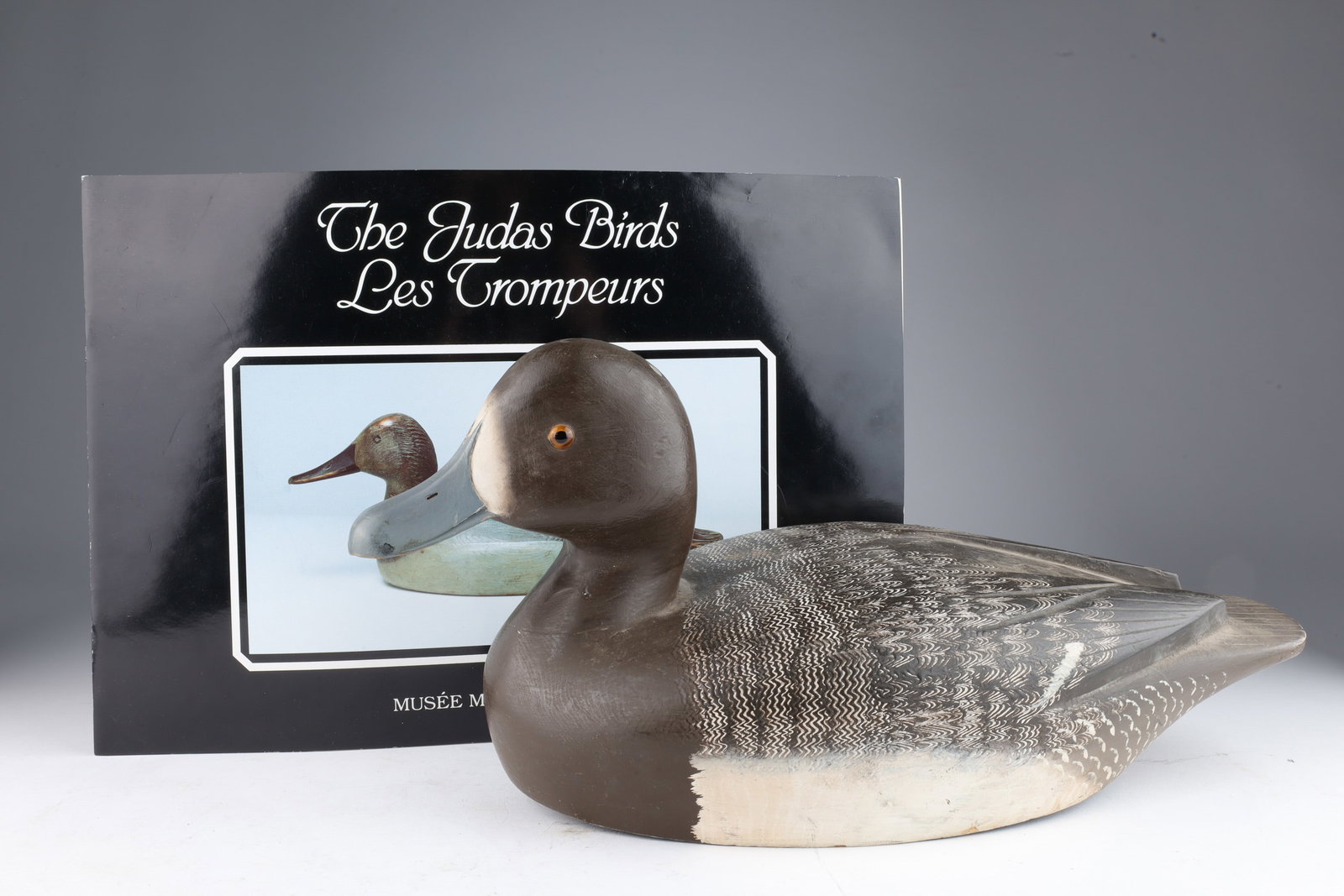 Carved Blue Bill Duck Decoy by Reg Bloom: Vintage Blue Bill Duck Decoy by Reg Bloom. Glass eyes, carved and painted feather details. Signed on base RGB. 13.25 inches L x 7 H x 5.5 W. Included as duck number 84, page 13 of the Judas Birds book