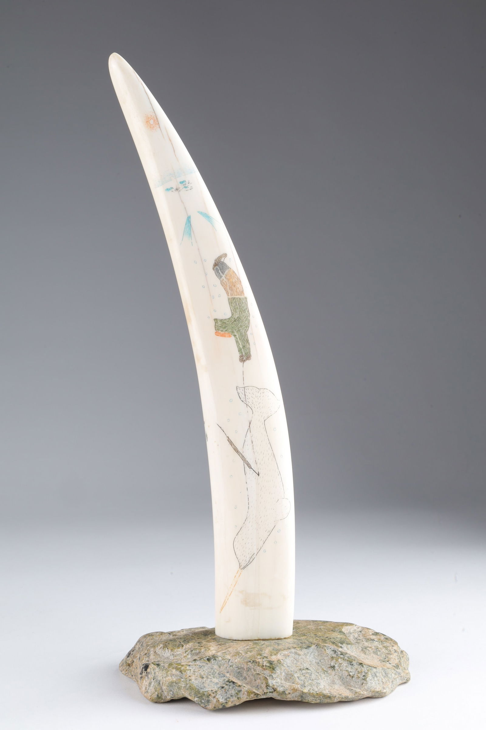 Signed Inuit Carved Scrimshaw, Hunt Scene: Signed Inuit Carved Polychrome Scrimshaw Walrus Tusk Depicting a Hunt Scene involving a Narwhal dragging a hunter underwater. Signed on tusk. Mounted on soapstone base. Measures 6 x 3.5 x 11.5 inches