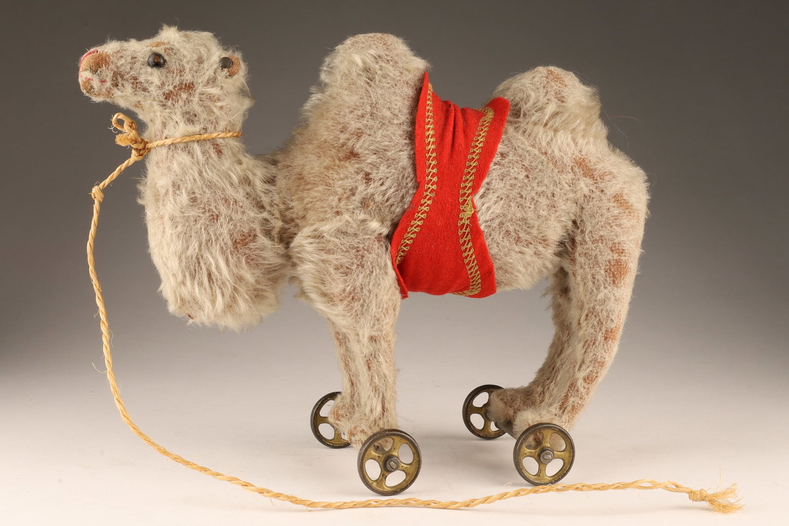 Antique Steiff Mohair Bactrian Camel on Wheels: Antique Steiff Mohair Bactrian Camel on Wheels Toy with black boot button eyes, red stitching, red saddlecloth with yellow stitching, gold-painted cast metal four-spoke wheels and Steiff button in ear