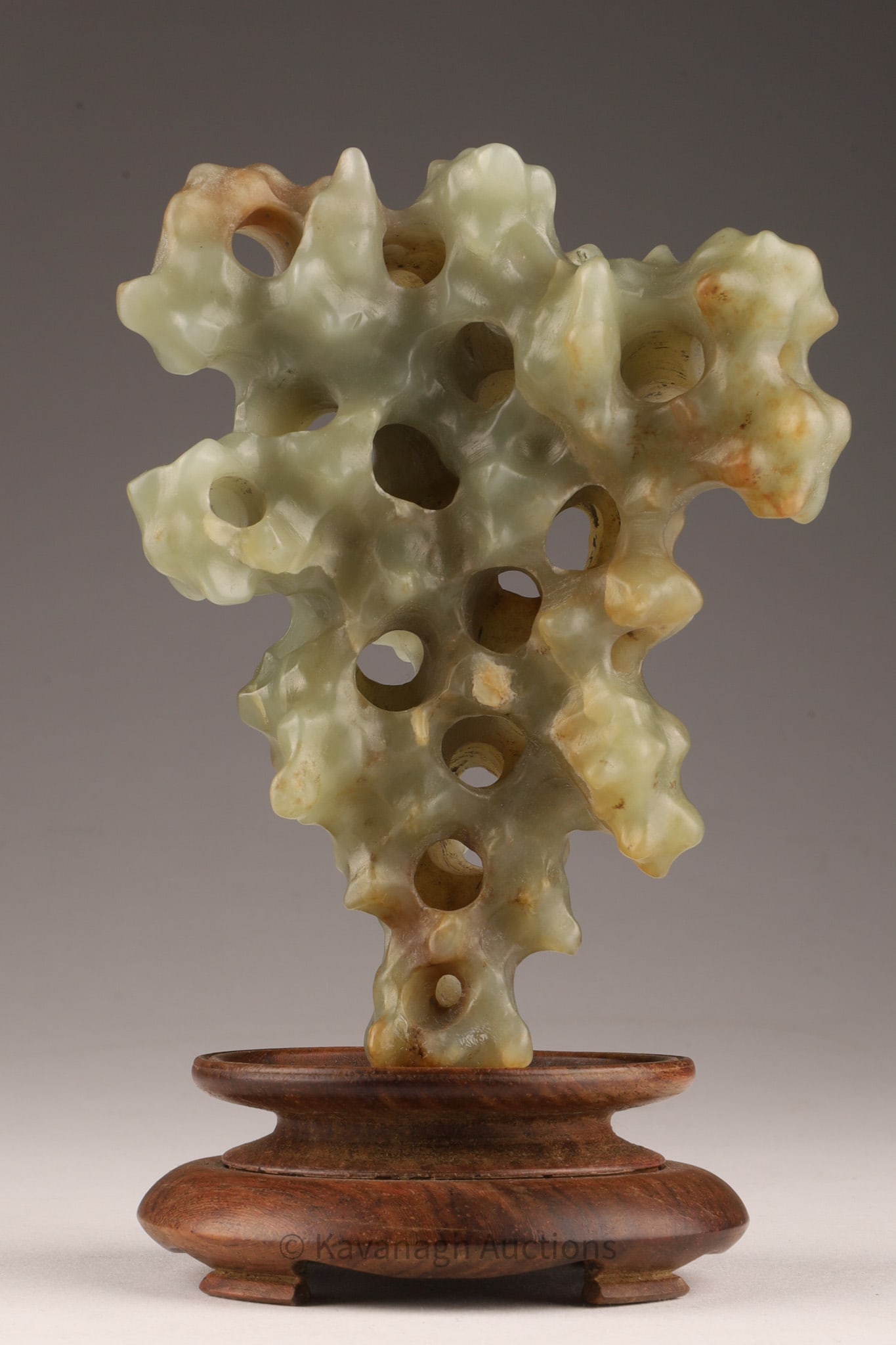 Chinese Mottled Celadon Hetian Jade Scholar's Stone: Chinese Mottled Celadon Hetian Jade Scholar's Stone / Rock. Carved pierced irregularly shaped vertical rockwork, mounted on wooden base, stone measures 5 inches H x 4 W, 6 inches H with base.