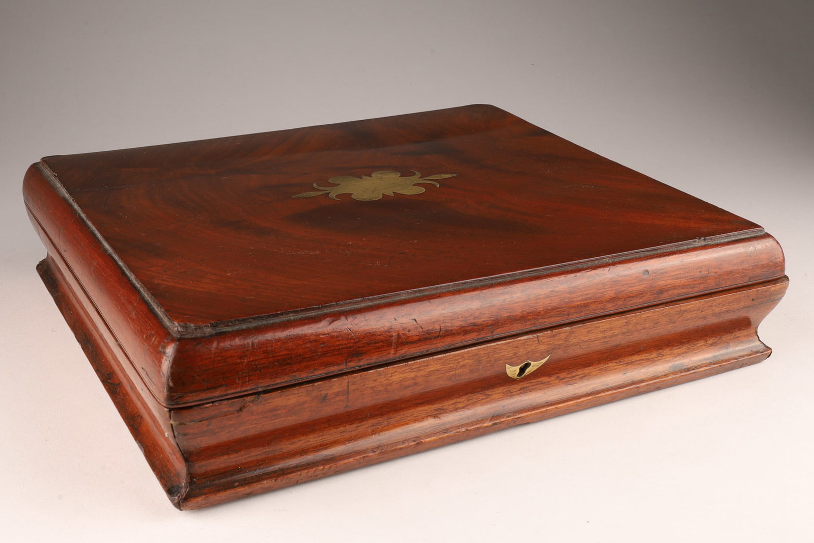 Antique Brass Inlaid Cutlery Box: Antique Brass Inlaid Cutlery Box with shaped sides and faded red velvet interior. Box is warped, measures 11 inches W x 10 deep x 3 H.