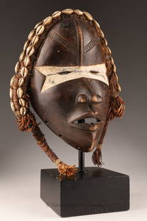 African Ivory Coast Dan Ceremonial Mask: African Ivory Coast Dan People Ceremonial Mask decorated with fibers and cowrie shells, on stand. Measuring 9.5 inches H x 8 W, 13 inches H on stand.