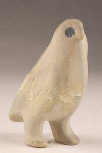 Inuit Stone Carving of a Standing Bird: Carved in a creamy beige stone with dark inlaid eyes, this small Inuit bird stands upright on two legs, its form simplified to essential contours. Areas of surface loss and wear reveal age and