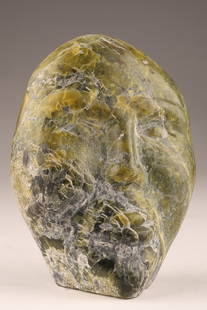 Inuit Stone Carving Human Face Plaque: Canada, mid-20th century hand-carved Inuit face plaque rendered in mottled green serpentine with grey-white veining. The stylized facial features?¢‚Ǩ‚Äùarched brows, nose, and parted