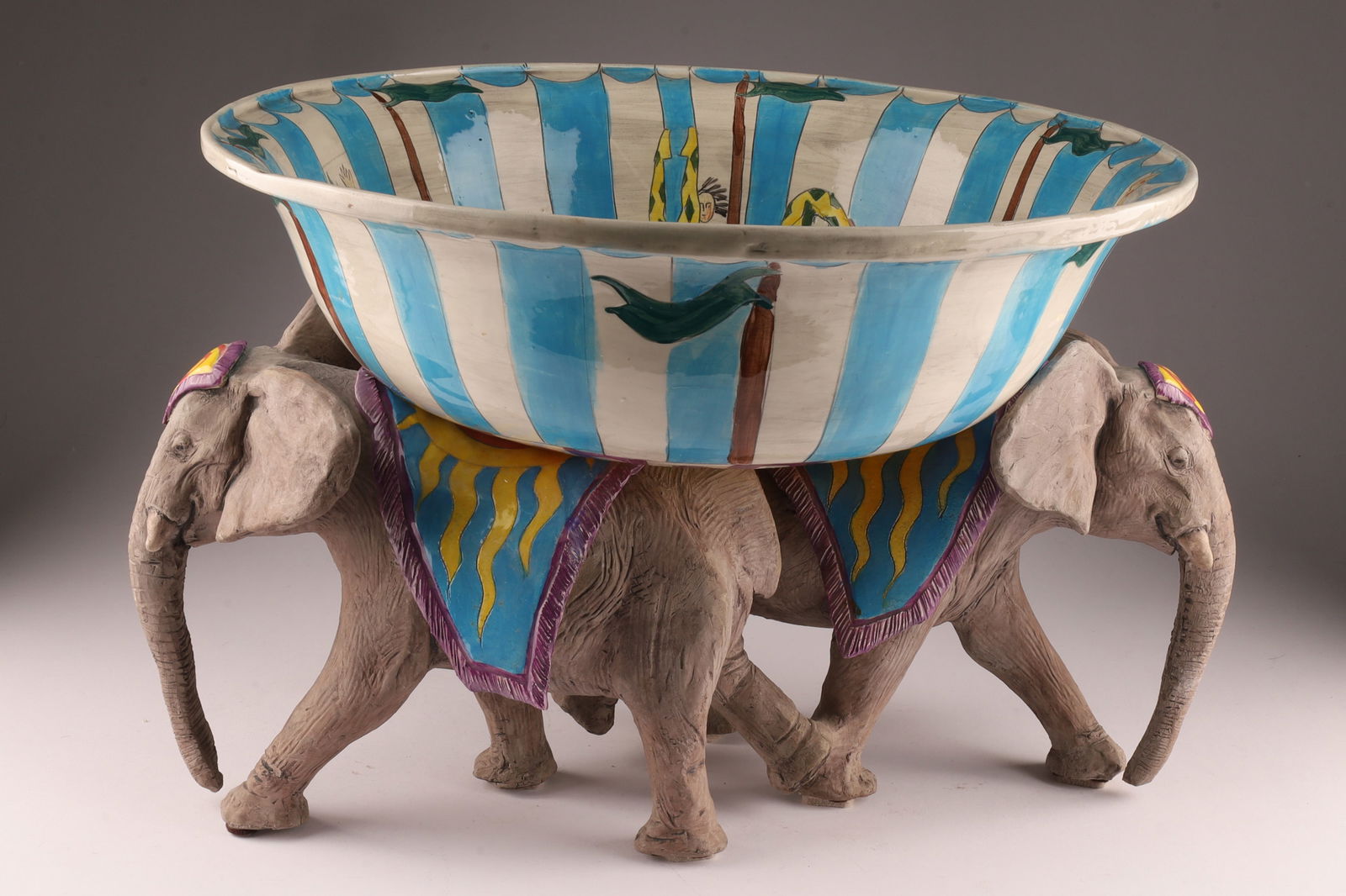 Dan and Nisha Ferguson Canadian Ceramic Circus Life Centrepiece Bowl: Dan and Nisha Ferguson (Canadian, b.1965 and 1966) Ceramic Circus Life Centrepiece Bowl composed of two elephants supporting a bowl, signed on foot. Measuring 18 inches W x 12 H with bowl.