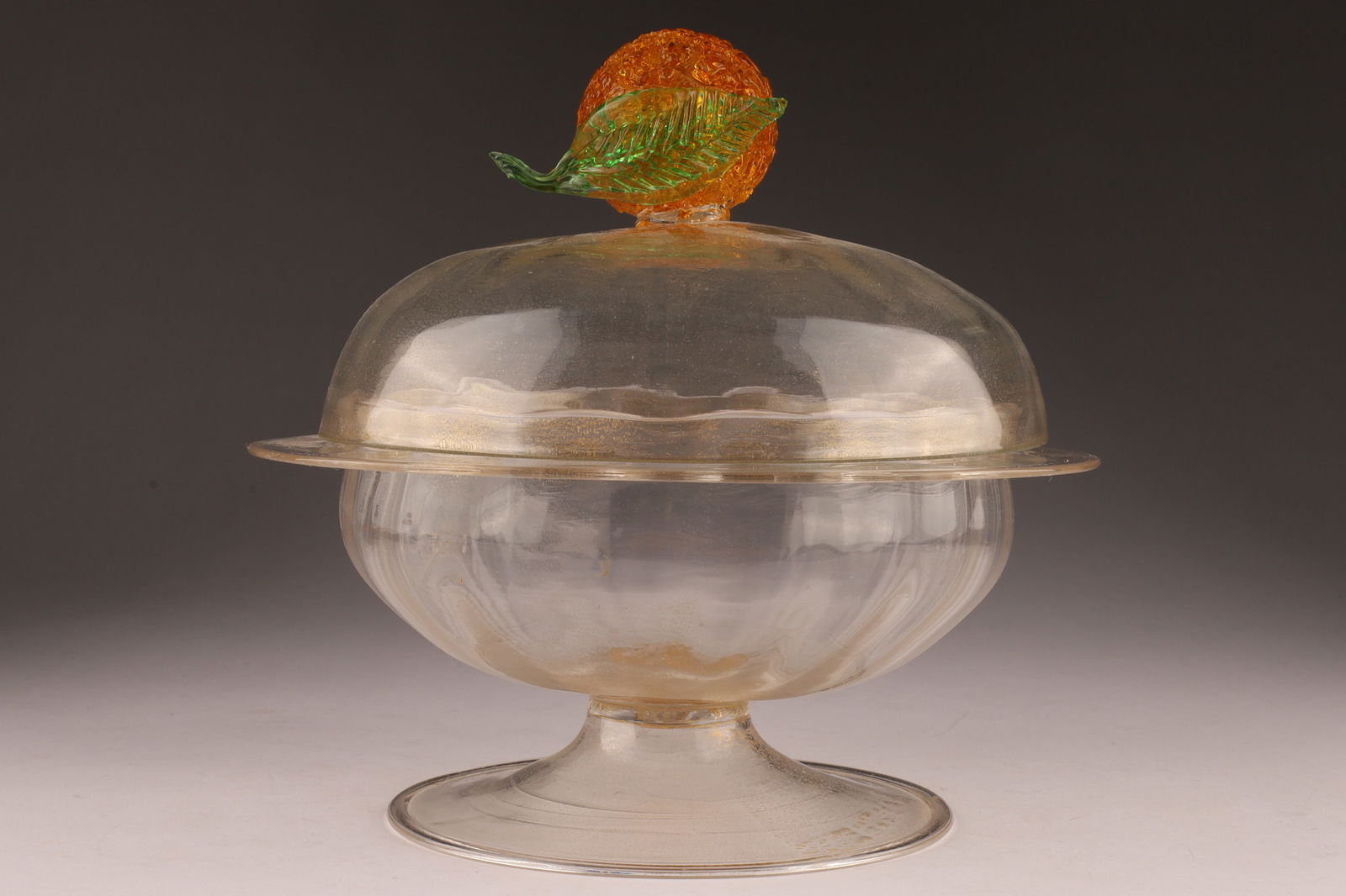 Venetian Murano Bowl and Cover with Orange Handle Gold Inclusions: Venetian Murano Ribbed / Costolato Bowl and Cover with Orange Handle and Two Green leaves, gold inclusions. Measuring 7 inches W x 7.5 H.