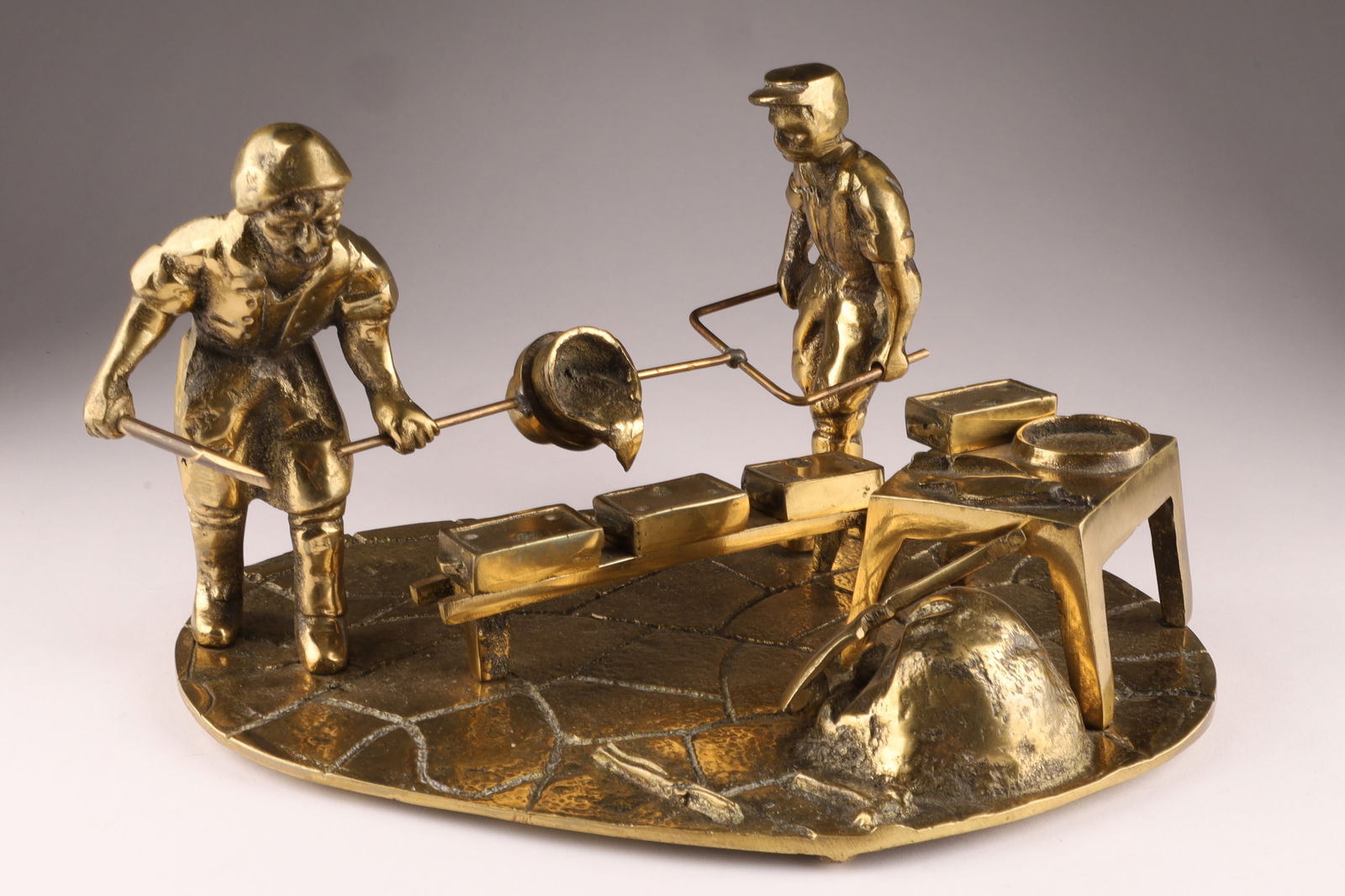 Antique Brass Figural Sculpture, Foundry or Blacksmith Scene: Antique Brass Sculpture Depicting a Blacksmith or Foundry Scene. It models a traditional workshop scene with figures using tools to pour molten metal into a mold. Hallmarked on the underside, D