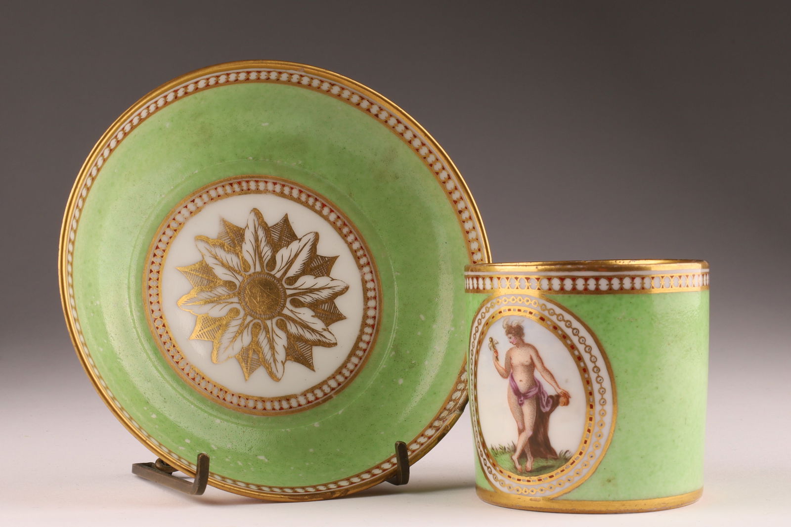 18th C Sevres France Porcelain Coffee Can and Saucer, Classical Scene: 18th C Antique Sevres France Porcelain Coffee Can and Saucer, with Classical Scene on green ground and gilt interior. Classical scene depicting a nude female with staff of Asclepius, possibly Hygieia.