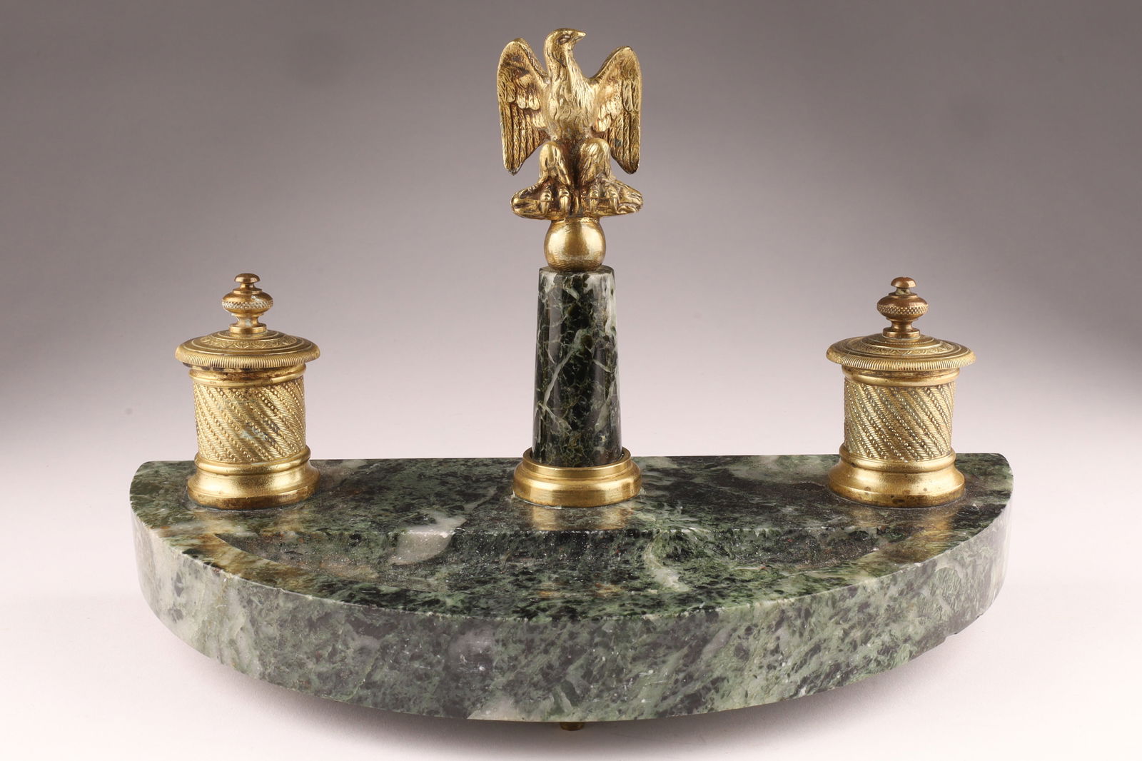Napoleon III Gilt Bronze and Verdi Alpi Marble Inkstand, France C. 1870: The crescent shaped and dished verdi alpi marble base mounted with a pair of lidded gilt bronze inkpots (glass wells absent) decorated with engine turned detail, centred by a marble column terminating
