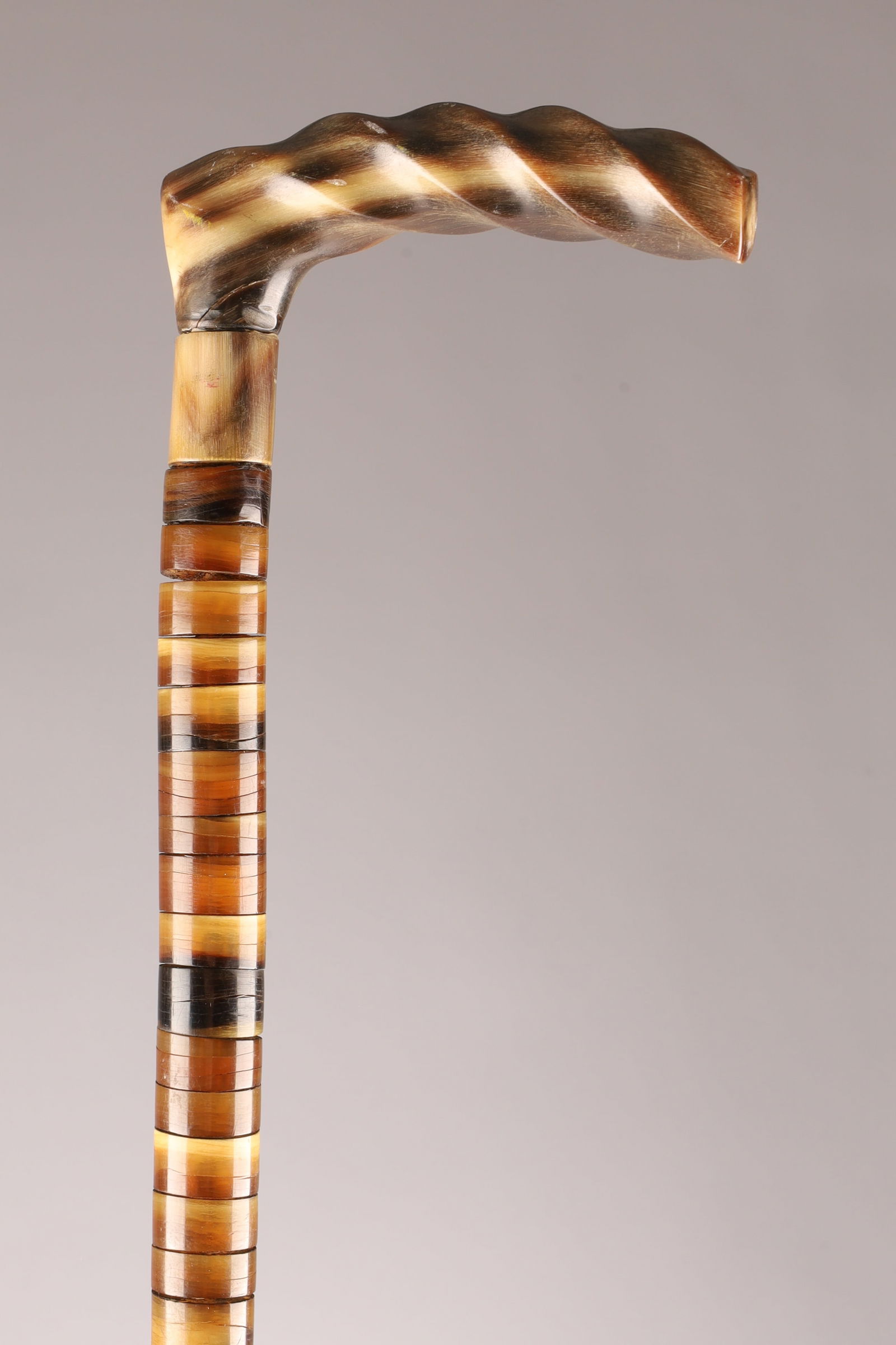 Antique Victorian Horn Walking Cane with Twisted Handle, 34.25 Inches: Antique Victorian walking cane crafted in horn, featuring a sculpted twisted handle and a finely constructed laminated horn shaft composed of stacked banded segments in alternating tones. The cane di