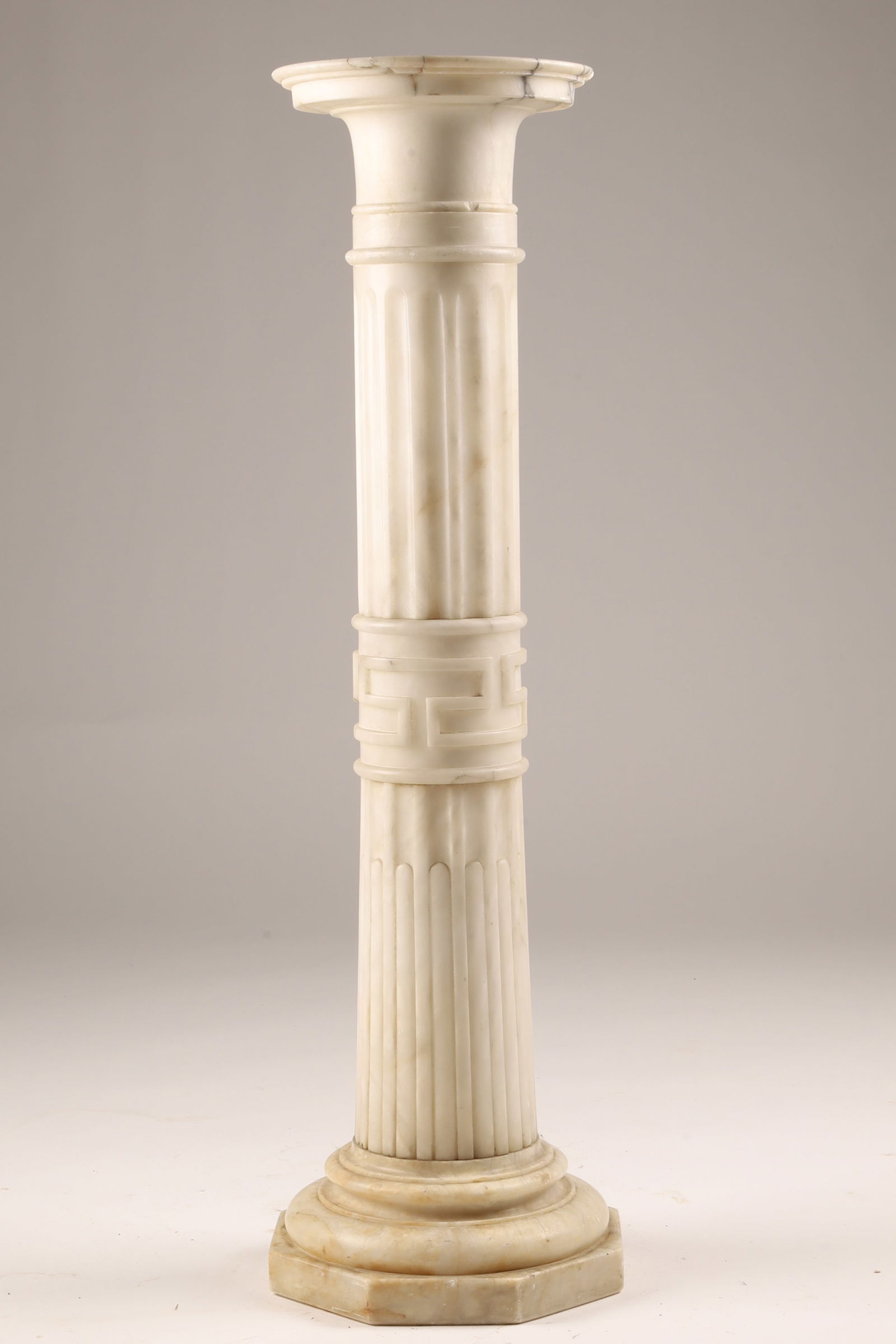 Classical White Marble Pedestal Column with Greek Key Motif: A classical-style white marble pedestal column featuring a fluted shaft and carved Greek key band to the midsection. The circular top rests above a molded collar and is removable, rotating freely on i