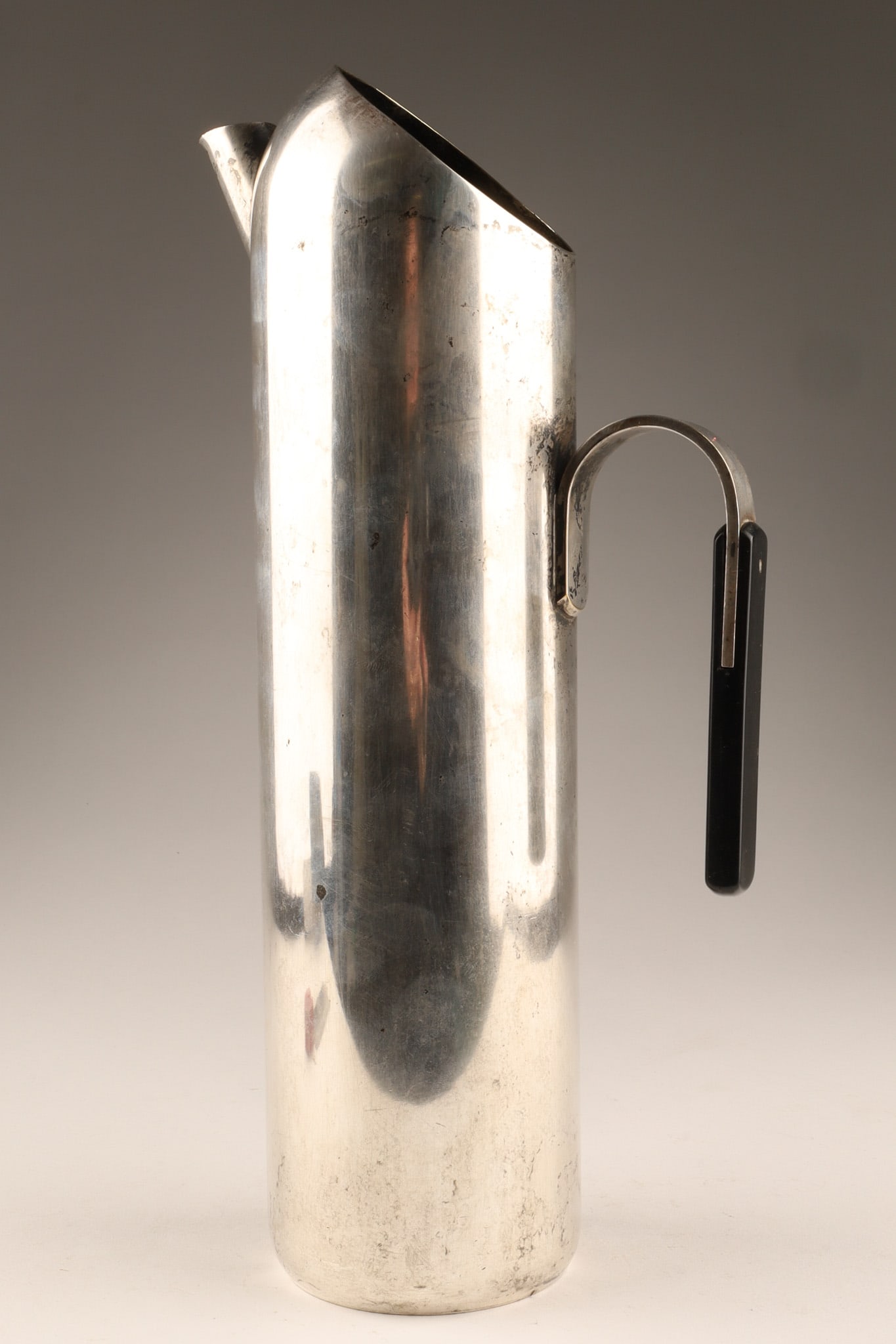 Mid Century Modern Italian Cocktail Pitcher: Mid-Century Modern cocktail pitcher, made in Italy. It features a sleek, tall cylindrical body with a black handle, marked Made in Italy on underside. Dimensions: 12 inches H x 5 W.