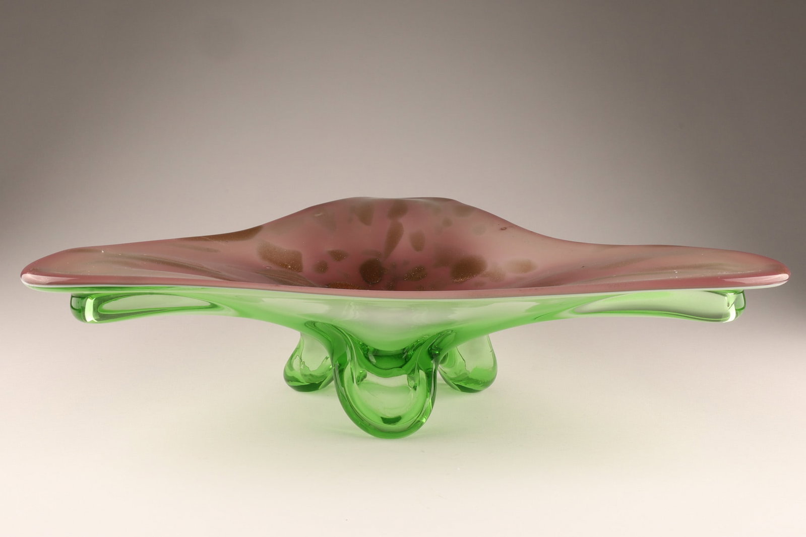 Mid Century Murano Sculptural Art Glass Bowl Aventurine c.1960: Murano sculptural centerpiece bowl of freeform triangular shape in translucent rose glass with gold aventurine inclusions, raised on integrated emerald green tripod support. Details Origin: Murano, It