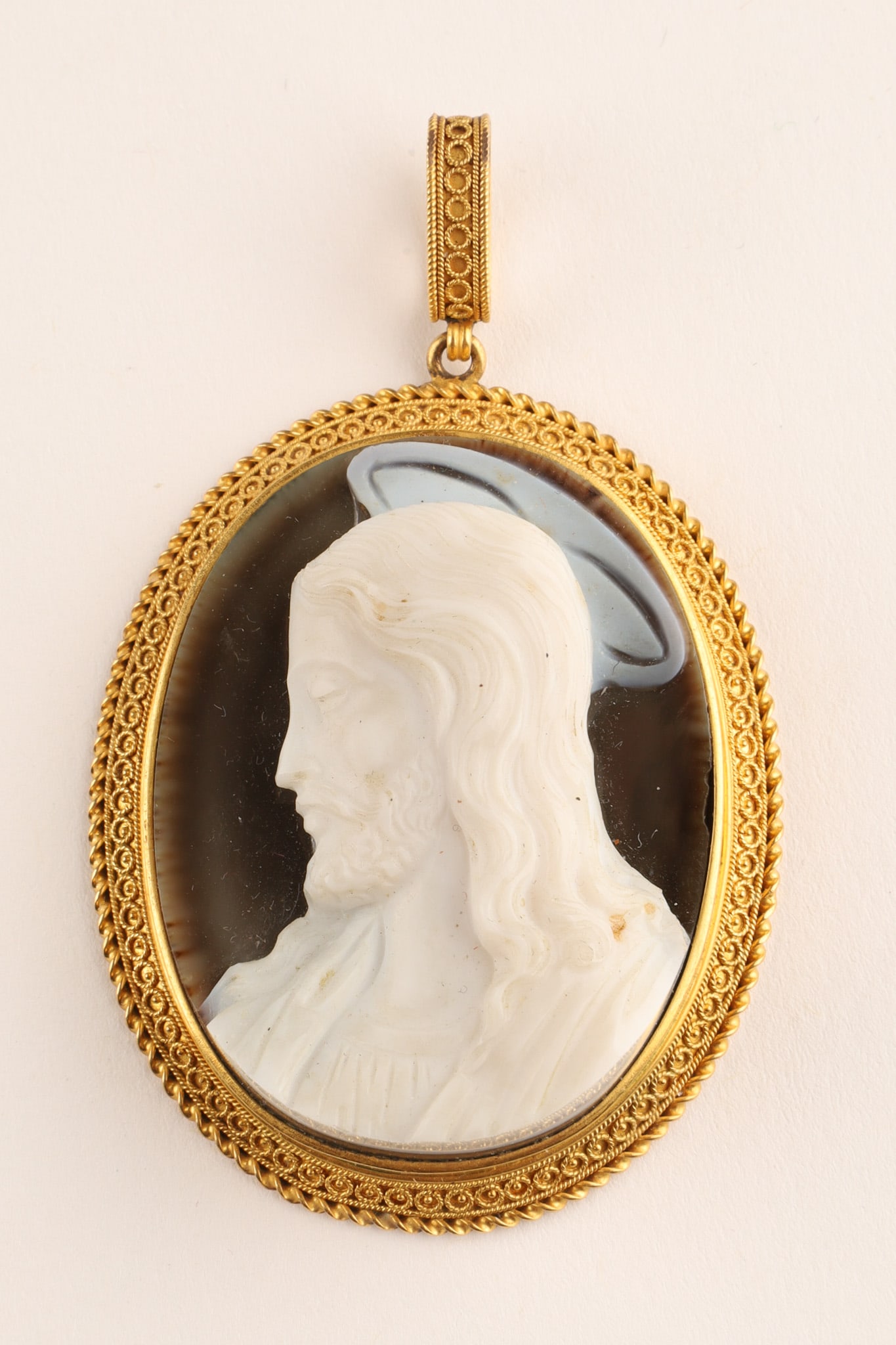 18K Gold Antique Cameo Pendant Profile of Jesus Christ: An 18 K Gold and antique cameo pendant featuring a profile of Jesus Christ. The white relief figure is set against a dark onyx background. Subject: Profile of Jesus Christ with a halo. Frame: The oval
