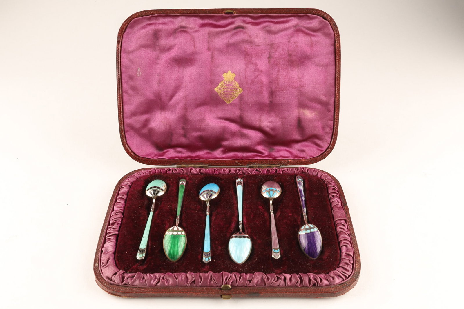 A Cased Set of Six Art Nouveau / Deco Sterling and Guilloche Enamel Coffee Spoons: A cased set of six guilloche enamel and sterling silver coffee spoons. Decorated in an Art Nouveau or Art Deco style. In a purple silk and velvet leather case, marked John Atterbury. John Atterbury wa