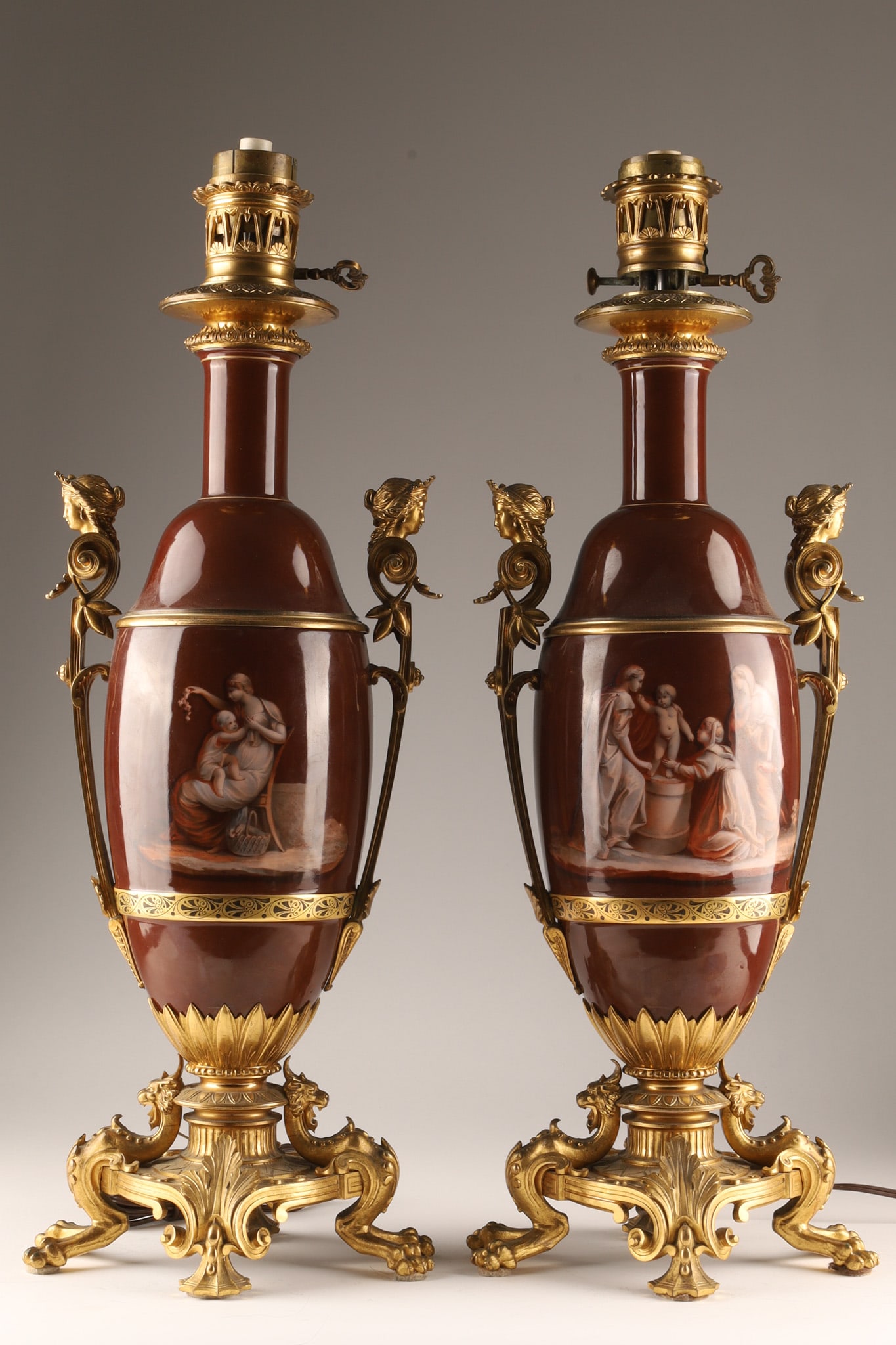 Antique French Neo-Classical Table Lamps, red porcelain with gilt bronze mounts: a pair of antique French Neo-Classical table lamps, red porcelain with gilt bronze mounts and painted Neoclassical figural scenes, featuring a deep reddish brown body mounted with ornate gilt bronze o