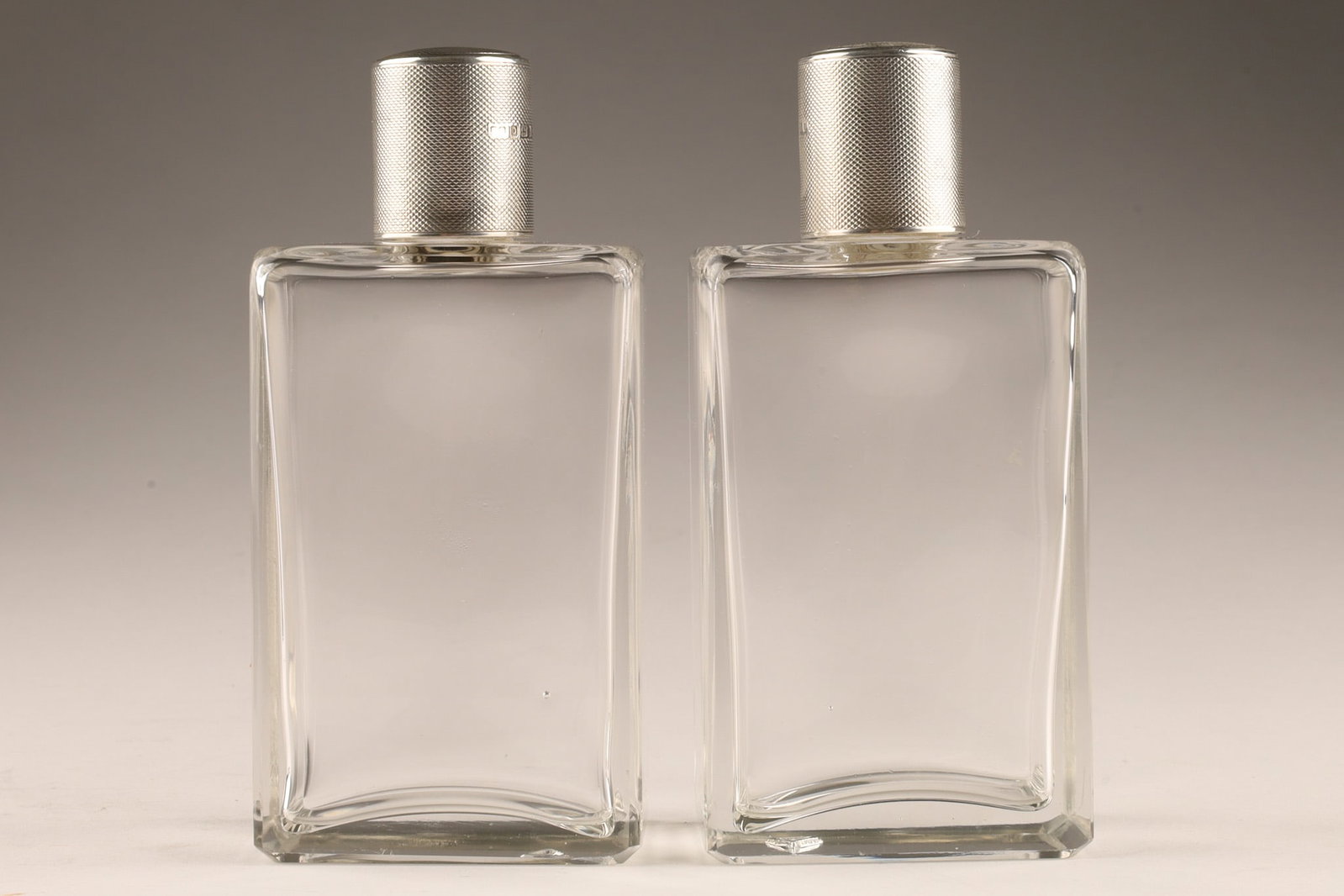Pair of English Art Deco Sterling Silver Mounted Perfume Bottles: Matched pair of English perfume bottles comprising rectangular cut-glass bodies fitted with engine-turned sterling silver caps. Dimensions: Approx. 4.5 in. (11.4 cm) .