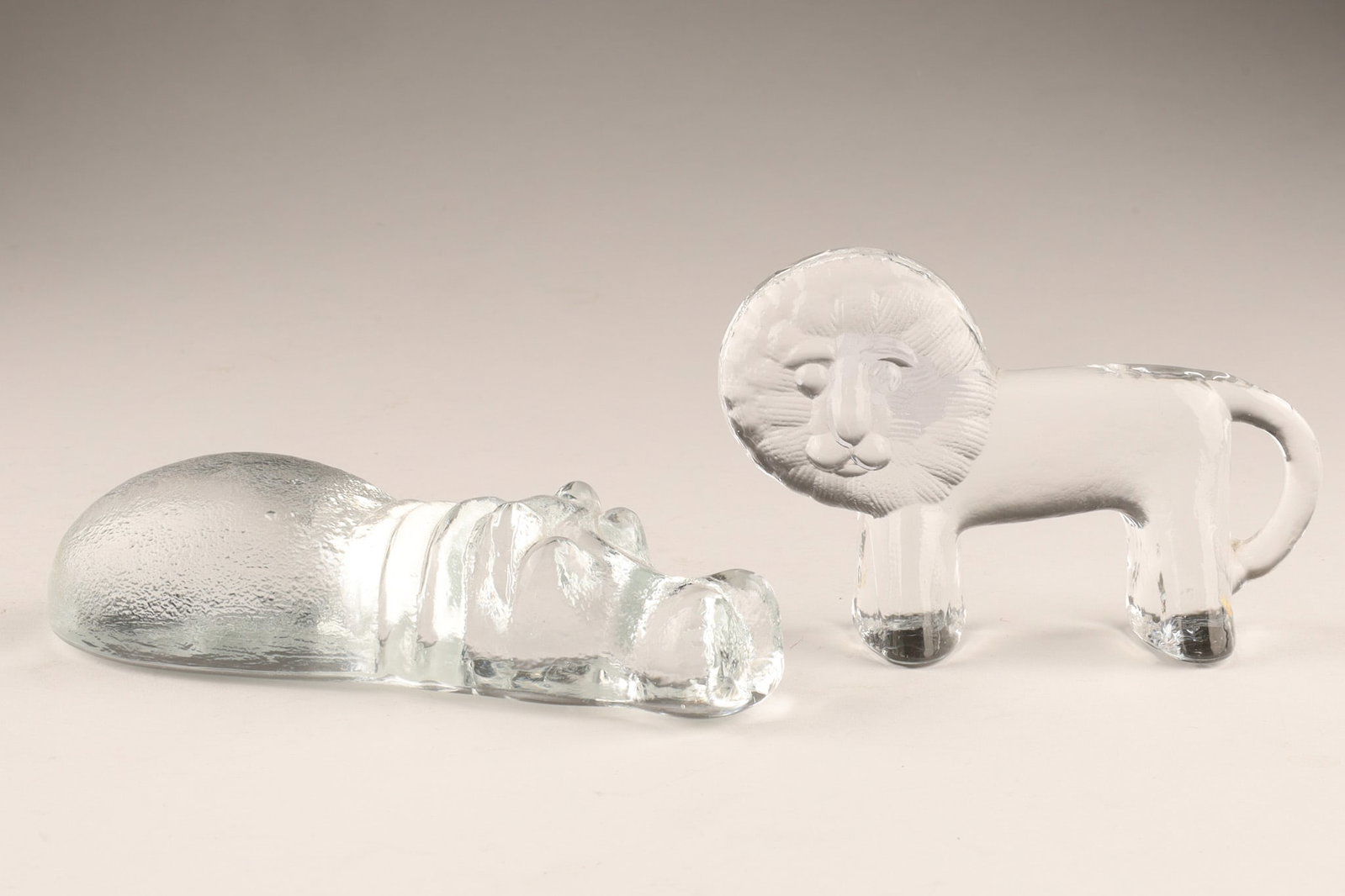 Kosta Boda Zoo Series Bertil Vallien Glass Animals, Lion and Swimming Hippo: A set of two Kosta Boda Zoo Series clear glass sculptures designed by Bertil Vallien in the 1970s. Dimensions: The lion measures 2.5 inches H x 4 W, swimming hippo measures 5 inches L x 2 W x 1.5 H.