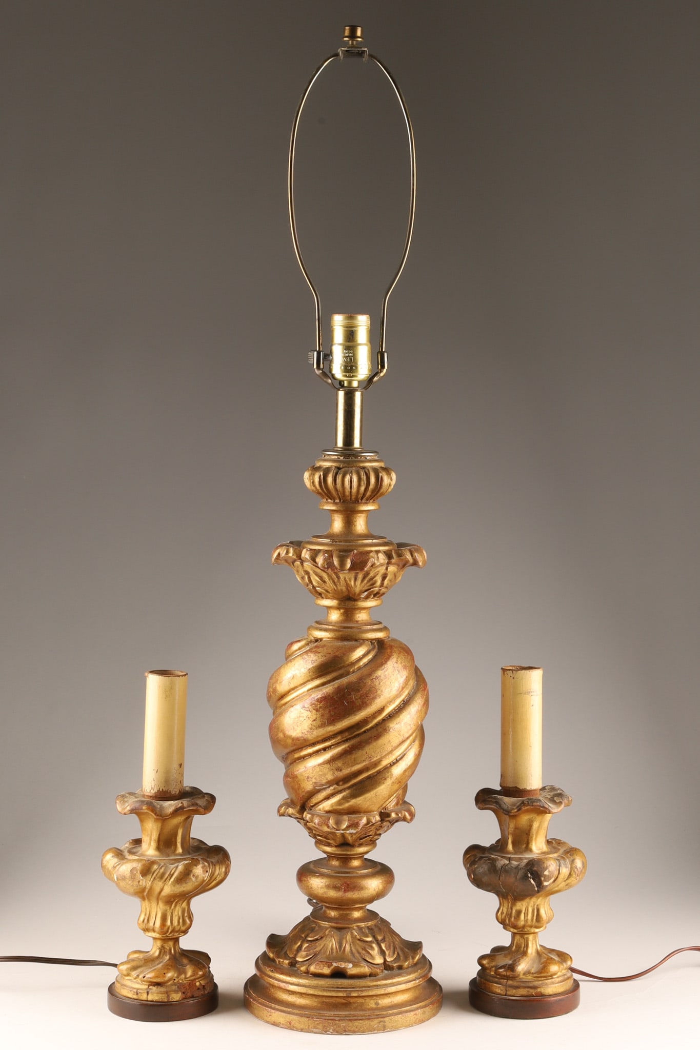 A Set of 3 Italian Baroque Style Giltwood Table Lamps: A pair of Italian Baroque-style candlestick table lamps and one urn lamp, constructed from giltwood, heavily inspired by Baroque aesthetics, featuring intricate carvings, ornamental scrollwork, and a 