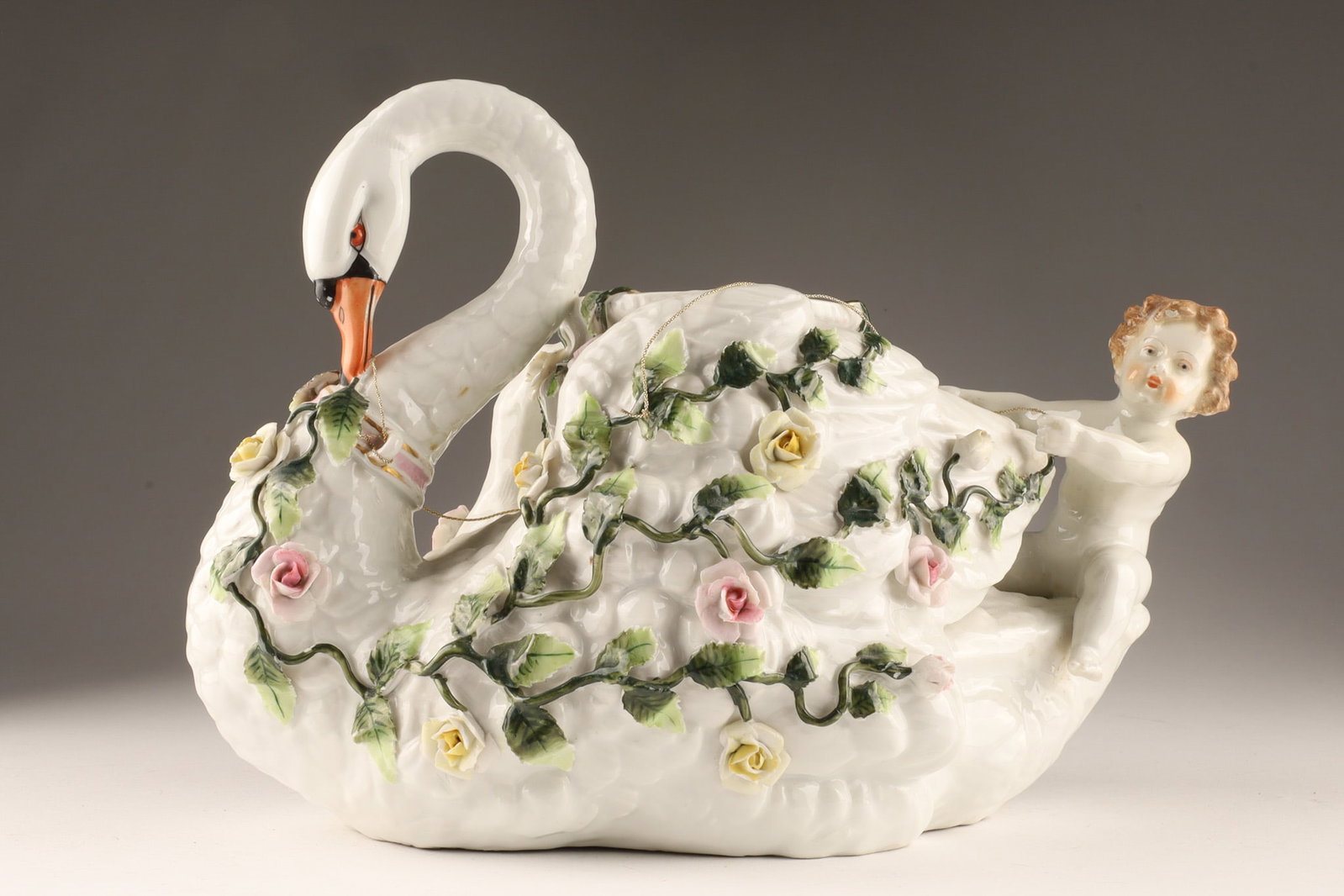 Antique German Porcelain Swan and Cherub Centrepiece Bowl: German porcelain swan and cherub centerpiece bowl, featuring a prominent white swan with an orange beak, wrapped in climbing relief vines, leaves, and delicate floral blossoms. On the rear tail of the