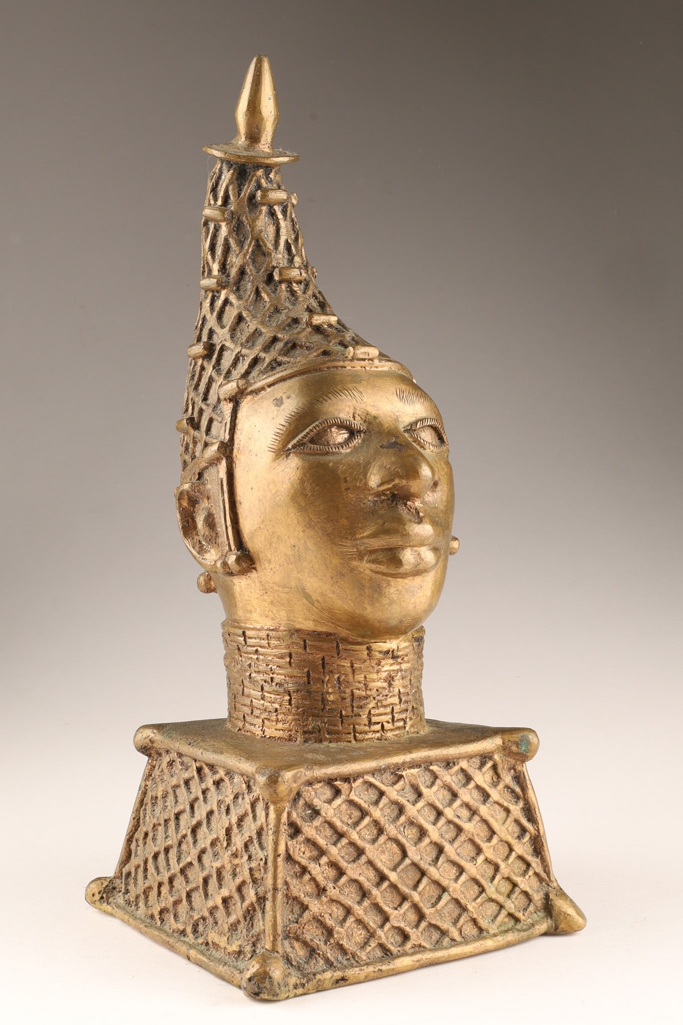 African Benin Bronze Commemorative Head of an Oba / King: A Benin bronze commemorative head of an Oba (king), featuring an elaborate conical headdress and a high collar of coral beads.These sculptures were crafted using the lost-wax technique to honor the di