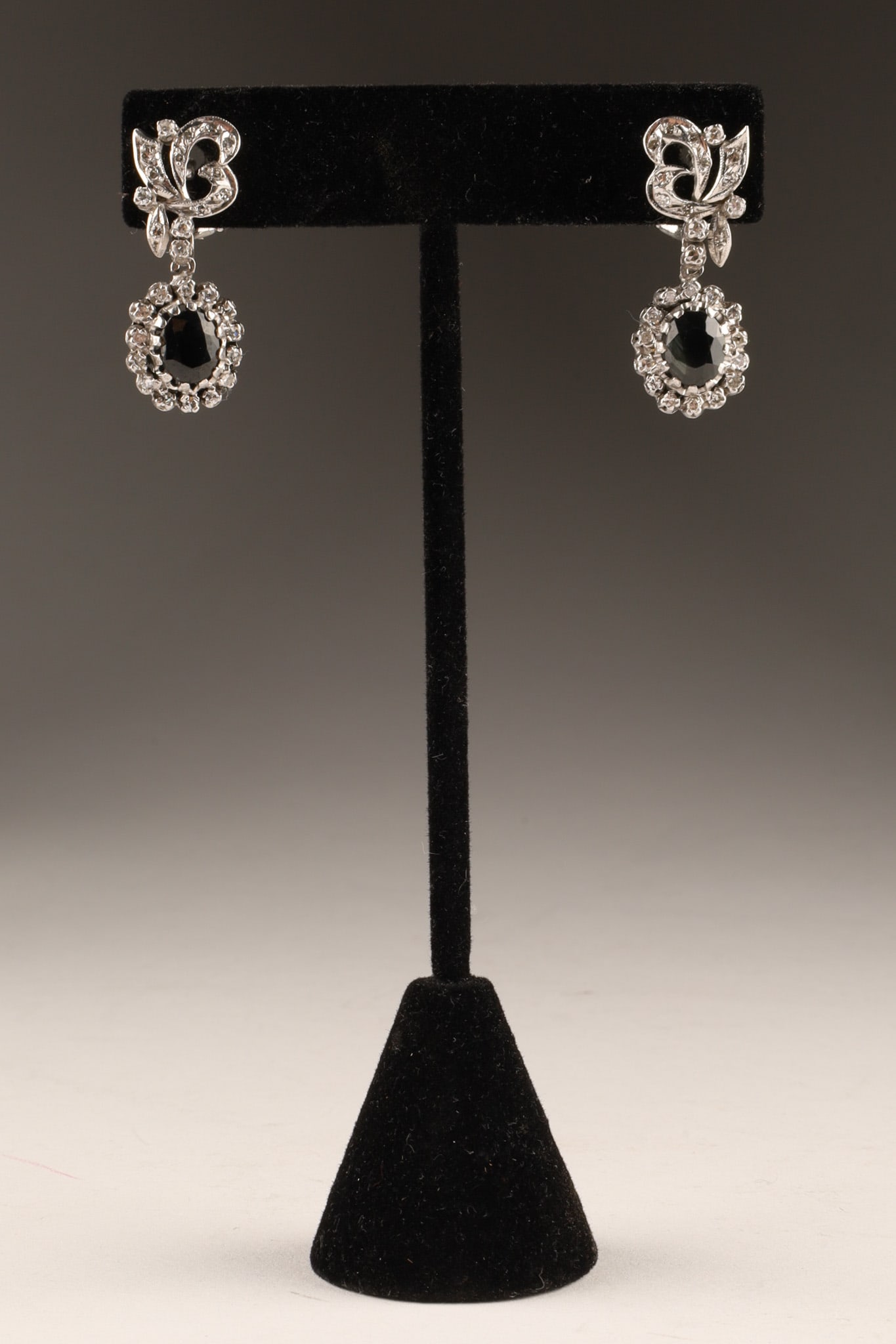 14k White Gold Diamond and Sapphire Dangle Pendant Earrings: A Pair of 14K White Gold, Australian Blue Sapphire, and Diamond Halo Drop Earrings. Designed for pierced ears, each earring showcases a central oval-cut Australian blue sapphire measuring approximatel