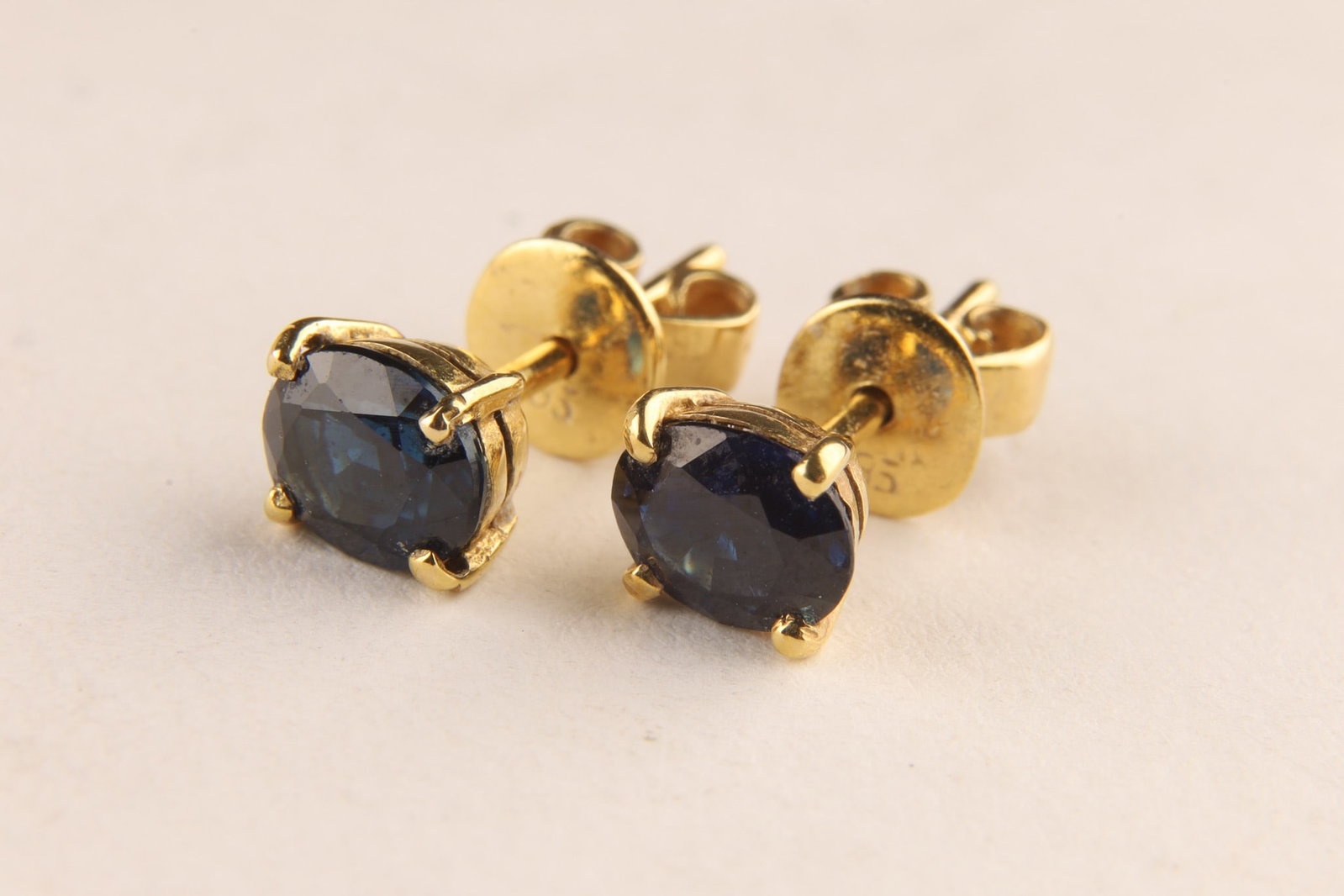 14K Yellow Gold and Sapphire Stud Earrings: A pair of 14kt yellow gold stud earrings set with 2 oval cut blue sapphires totalling 1.50 carats. With assorted friction backs for pierced ears. Total weight 1.6 grams. Accompanied by a certificate o
