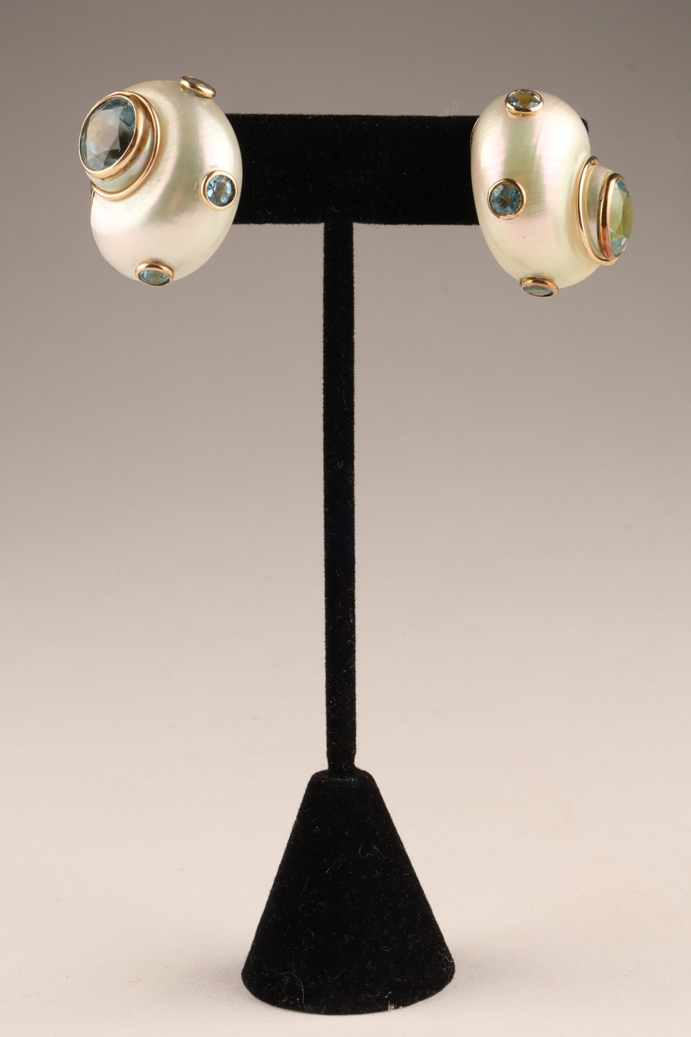 Mazza Mother of Pearl and Gem-set 14K Yellow Gold Shell Earrings: Each a turbo shell with a center bezel set round cut blue topaz (9.75mm), with bezel set blue topaz accents (3.7mm), and accented with gold rope twist wire wrap, completed with omega clip backs, stamp