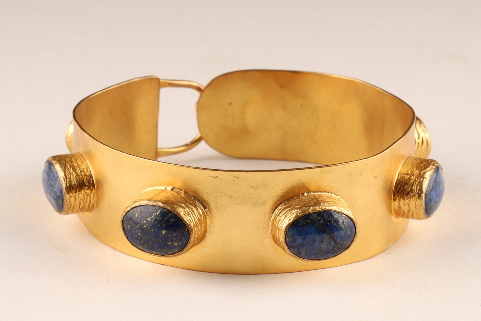 Byzantine Bangle Cuff Bracelet Gold Plated with Lapis Lazuli Cabochons: A Byzantine-inspired hand hammered statement cuff bracelet featuring a wide, structured gold-plated band, the exterior is punctuated by 7 prominent, bezel-set oval lapis lazuli cabochons displaying a 