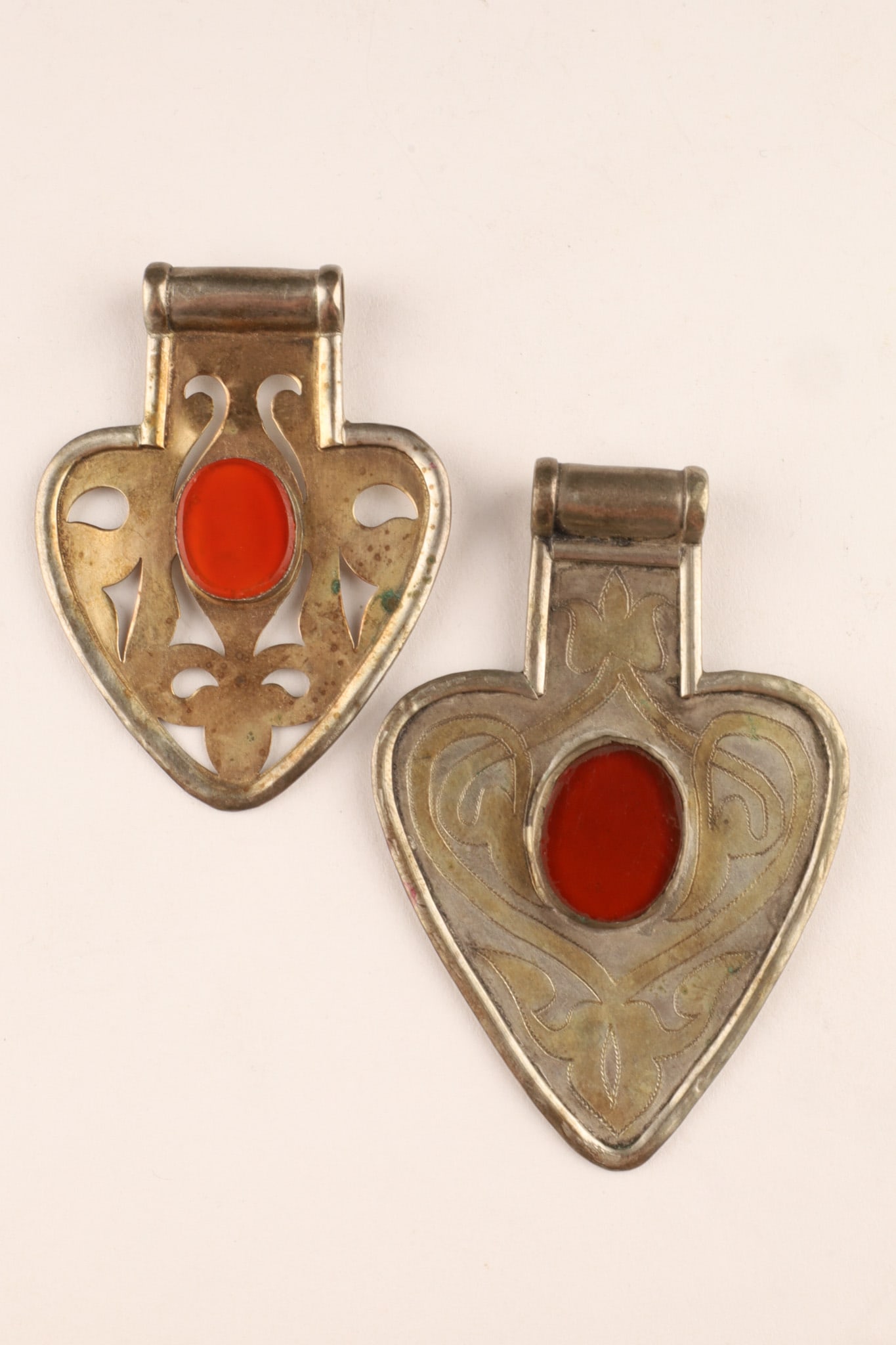 Pair of Antique Turkmen Silver and Carnelian Heart Shaped Pendants: An pair of antique Turkmen heart-shaped (asyk or ashik) pendants, featuring a central, bezel-set carnelian cabochon, framed by hand-engraved and pierced abstract openwork motifs. Larger measures 3 inc