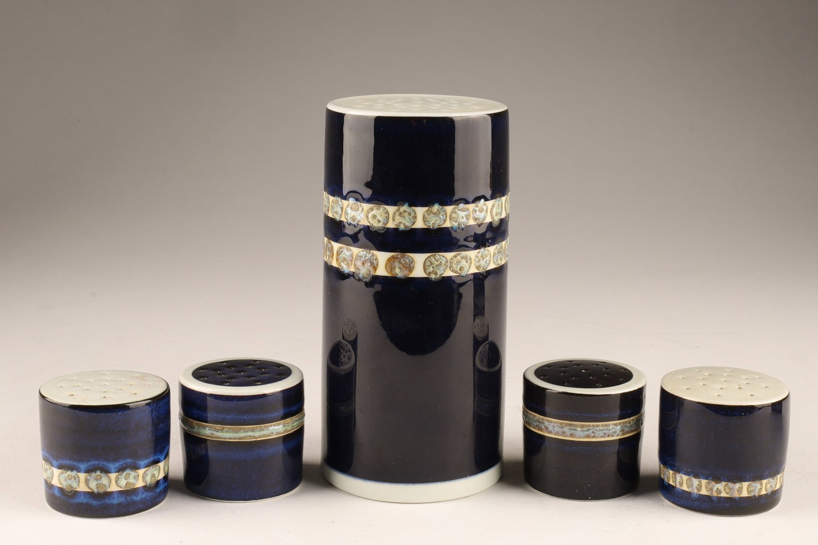 MCM Royal Copenhagen Tenera Fajance Shaker Set by Inge-Lise Kofoed: The set includes a tall sugar sprinkler/shaker and four smaller salt or pepper shakers, featuring a distinct blue and white faience ceramic with a detailed pattern band. Originally produced by Alumini