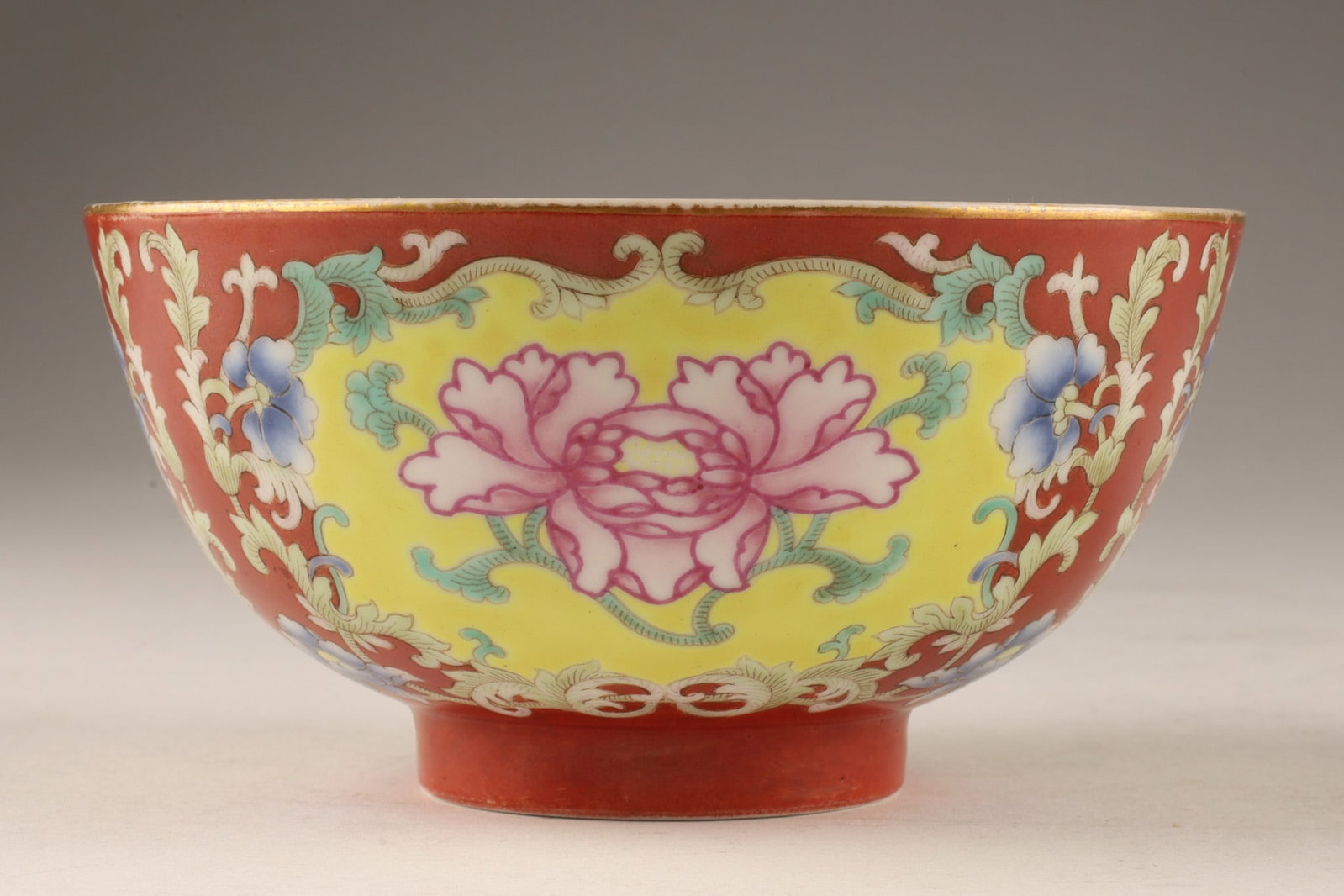 Chinese Coral-Ground Famille Rose Peony Porcelain Bowl, 20th C: A Chinese coral-ground famille rose peony porcelain bowl enameled in famille rose with shaped yellow-ground cartouches enclosing blossoming pink peonies amidst leafy tendrils and blue floral accents. 