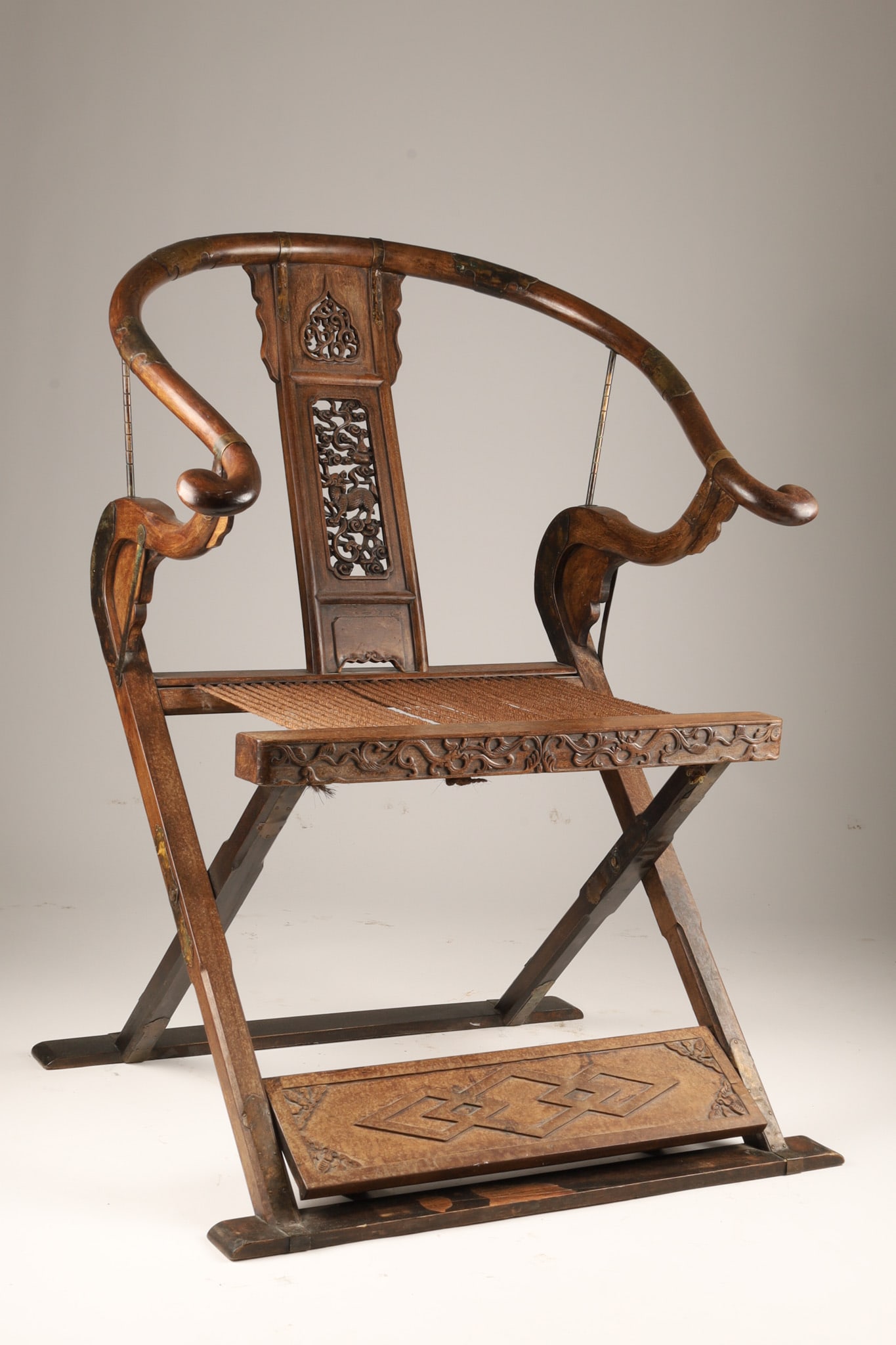 Antique Chinese Horseshoe-back Folding Throne Chair: An antique Chinese horseshoe-back folding throne armchair or jiaoyi, featuring a curved crest rail, an intricately carved back splat, a rush seat, and a hinged X-frame design and foot rest. Measuring 