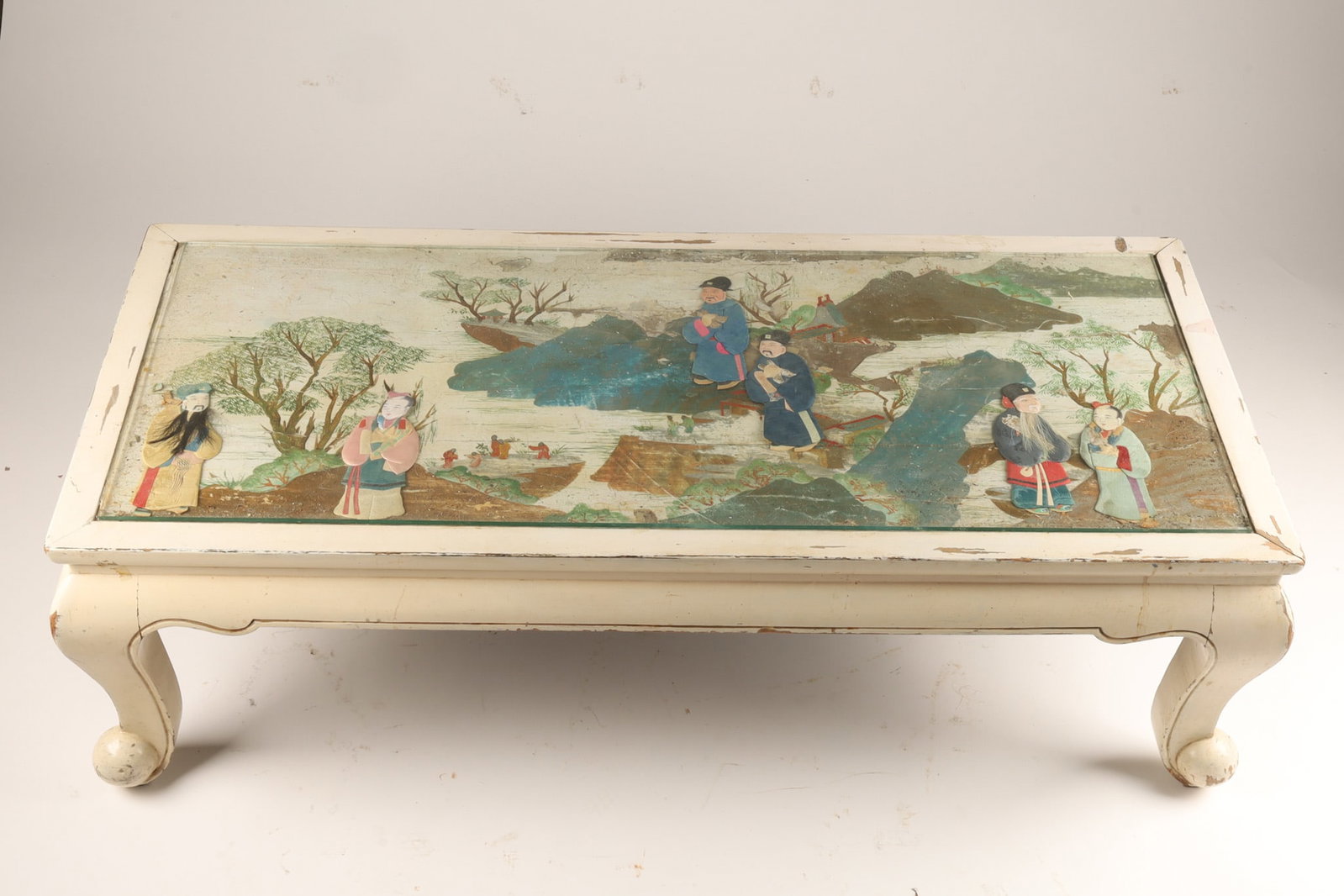 Asian / Chinese White Coffee Table, Paper Figures in Painted Landscape: A vintage low coffee table featuring a painted landscape scene with paper doll style figures, set within a white painted wooden frame with curved cabriole-style legs. 22 inches deep x 48 L x 17 H.