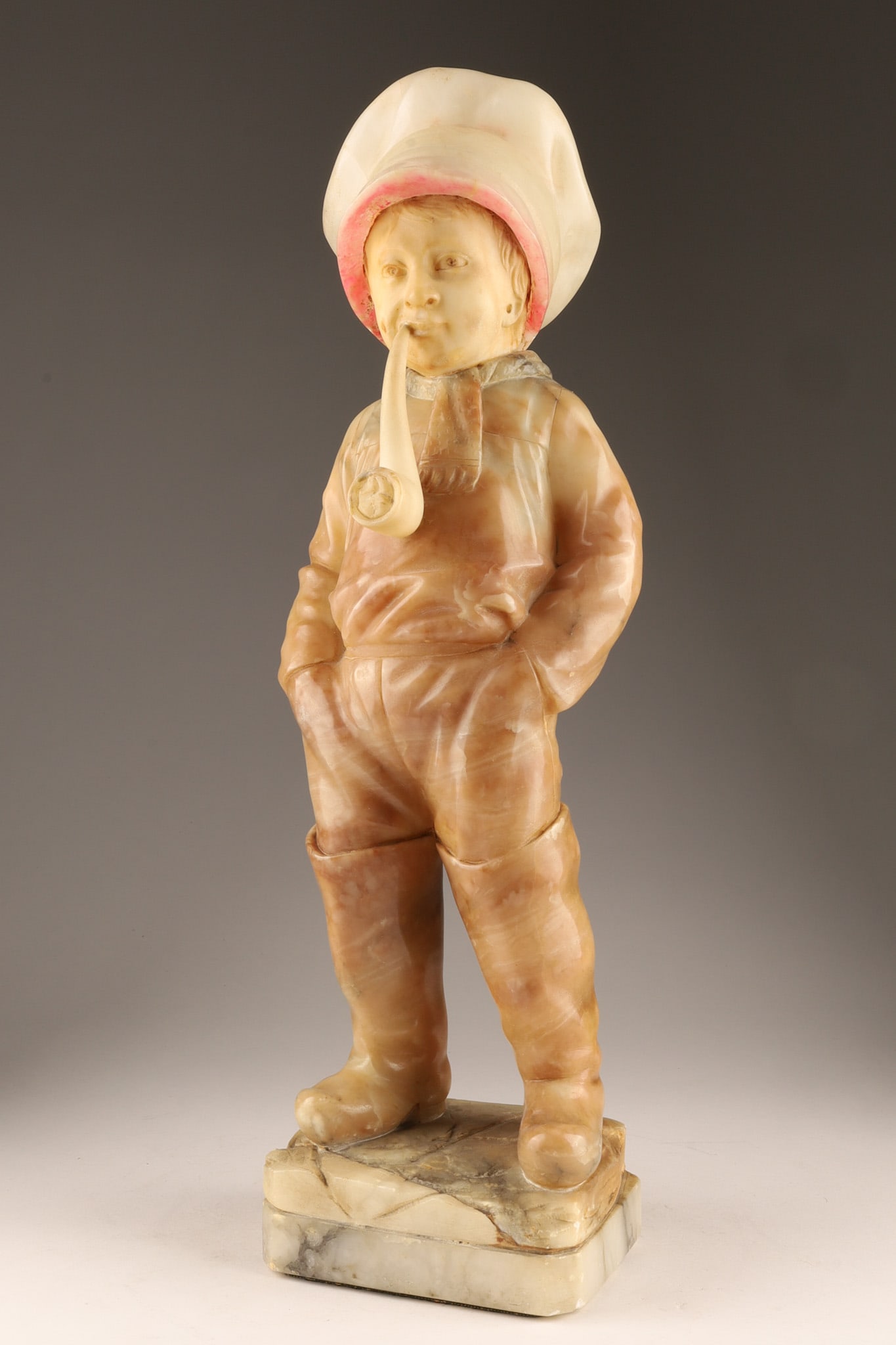 Art Deco 1930s French School Comme Papa Alabaster Sculpture: Art Deco French School carved alabaster and polychrome sculpture titled Comme Papa. The figurine depicts a boy wearing a large cap and boots while smoking a pipe. Measuring 20 inches H x 7 W x 5.5 dee