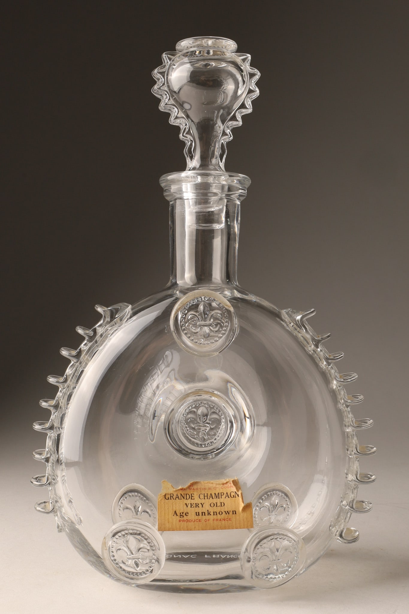 Remy Martin Louis XIII Grande Champagne Cognac crystal decanter: Remy Martin Louis XIII Grande Champagne Cognac crystal decanter, featuring distinctive fleur-de-lis spikes and a matching stopper. With original paper label, chip to one spot on lower left. 11 inches 