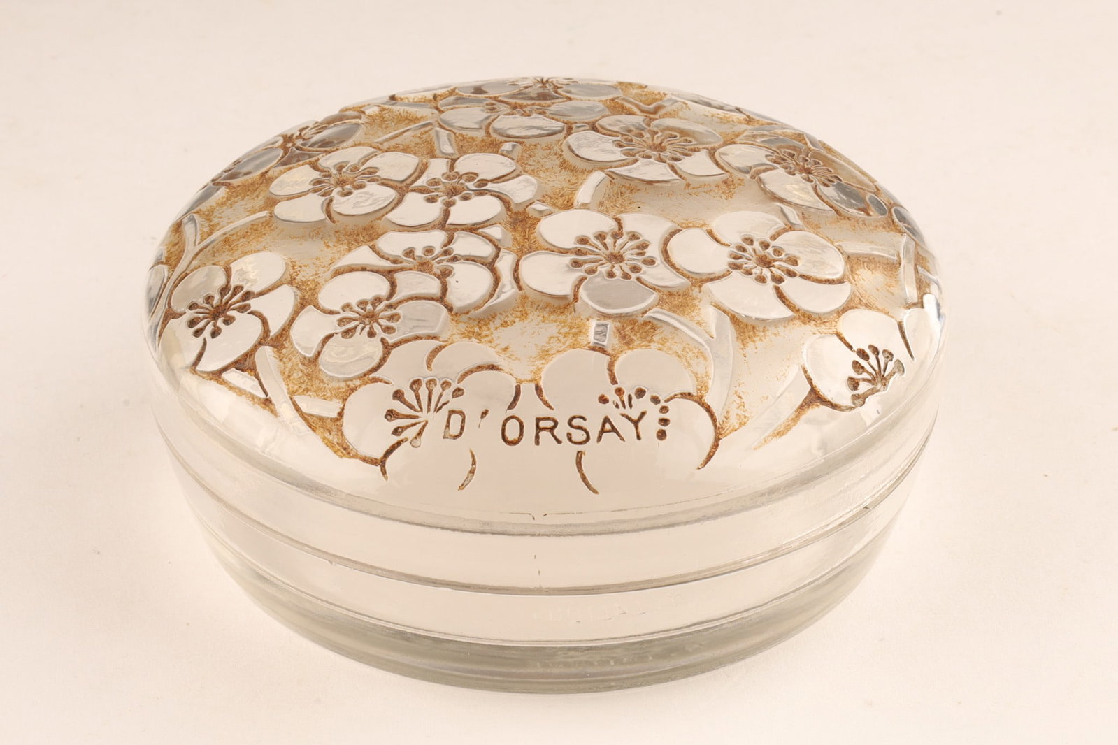 Rene Lalique Le Lys for D’Orsay Dresser Box c.1922: An antique 1920s Rene Lalique Le Lys powder box made for D'Orsay, featuring frosted glass with a sepia patina finish. The lid is molded with a relief pattern of flowers and branded D'ORSAY. 4 inches d