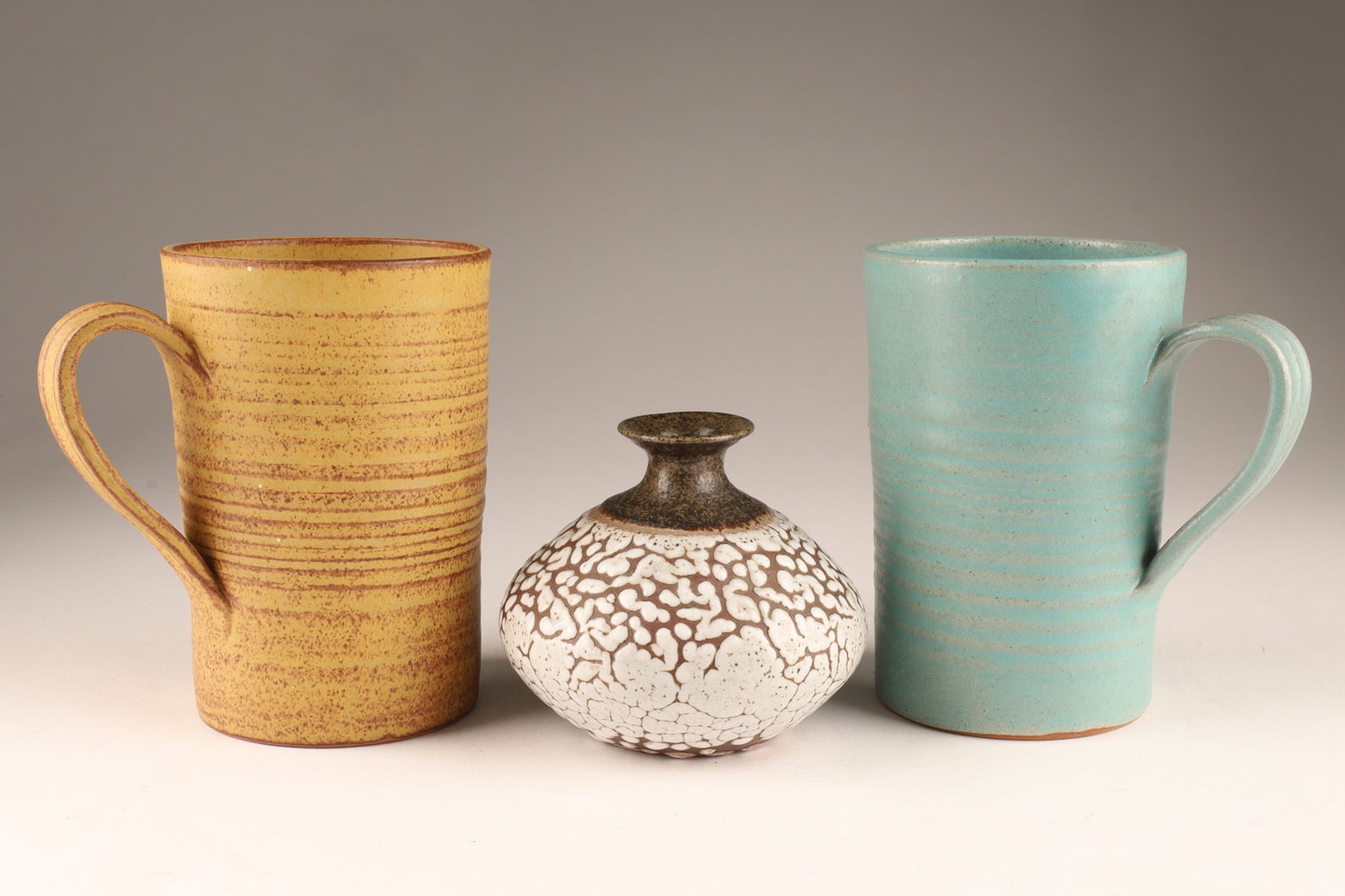Pair Kjeld and Erika Deichmann Canadian Art Pottery Mugs with Small Vase: A Deichmann Pottery set featuring two distinct tall, ribbed cylindrical mugs and a central small Snow-on-the-Mountain textured crackle-glaze vase. Handcrafted in New Brunswick by Kjeld and Erika Deich