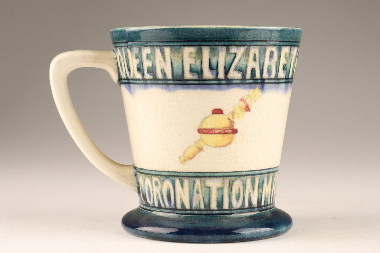 1937 Moorcroft Commemorative Coronation Mug of King George VI and Queen Elizabeth: A 1937 Moorcroft mug designed by William Moorcroft to commemorate the coronation of King George VI and Queen Elizabeth. It features a conical shape with Royal emblems placed between bands of text. The