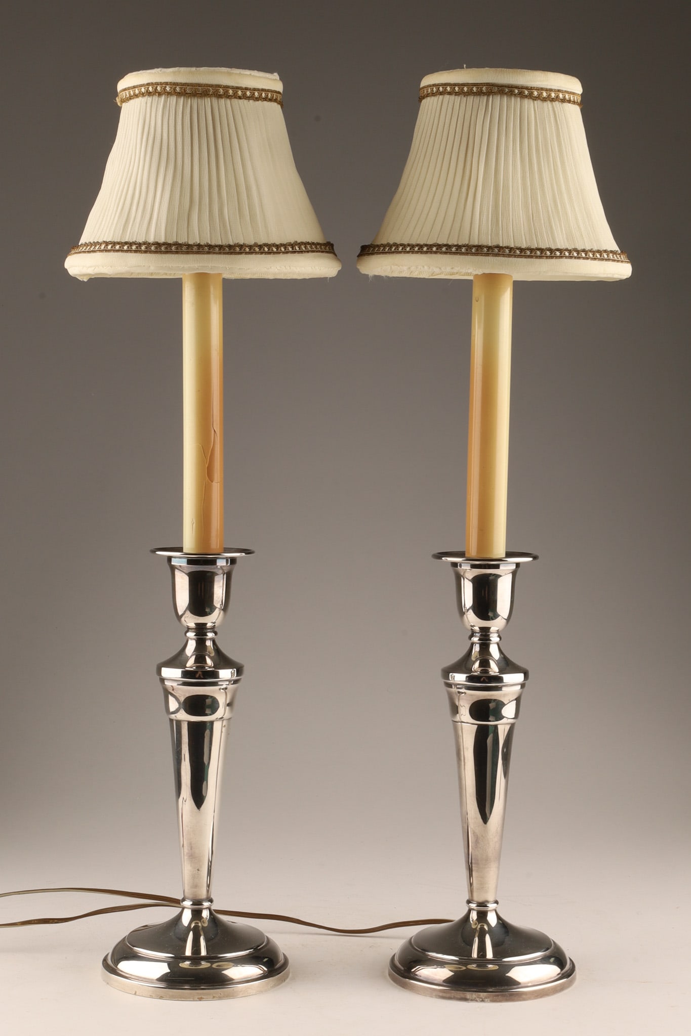 Pair of Antique Silver Plated Electrified Candlestick Buffet Lamps: A pair of antique silver-plated candlestick buffet lamps featuring classic, elegant fluted pillars resting on circular stepped bases. Originally styled as traditional candlesticks, they have been conv