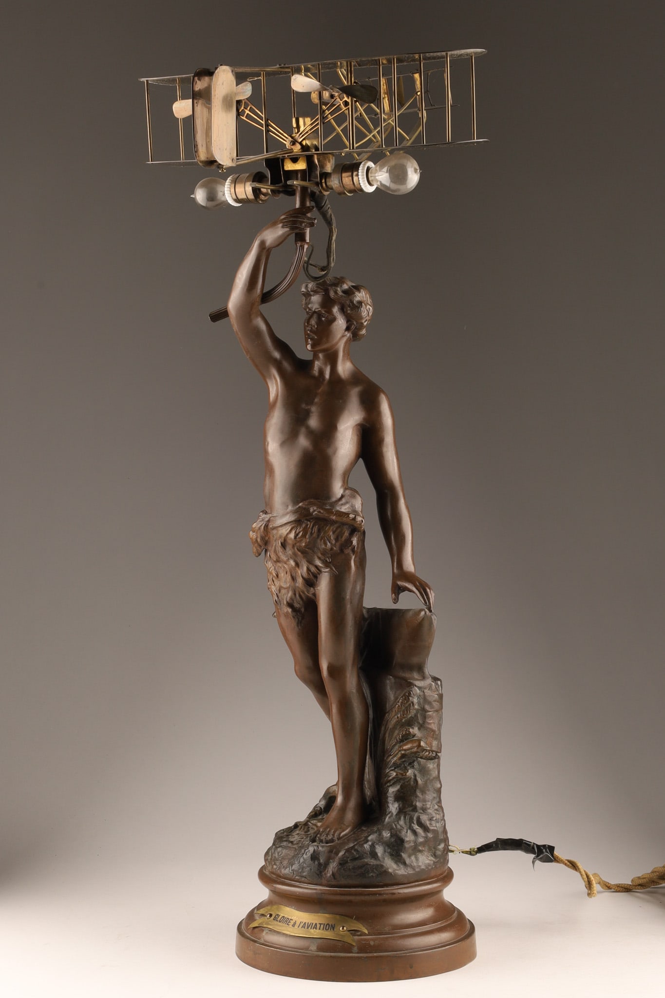 Gloire a L'Aviation Spelter and Brass Lamp / Figural Sculpture: Gloire a L'Aviation Spelter and Brass Lamp featuring an antique figural sculpture featuring a patinated bronze-finish classical male figure standing on a rocky base and holding aloft a biplane-shaped 