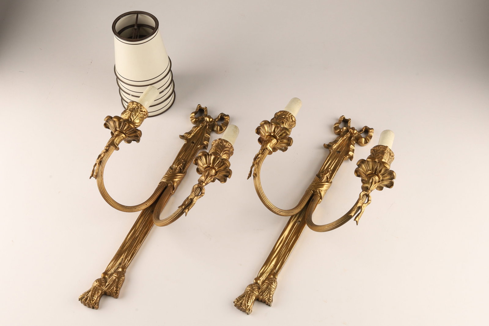 Pair French Cast Bronze Or Brass Wall Sconces, Louis XVI Or Neoclassical Style: Pair of French cast bronze or brass wall sconces, in the Louis XVI or neoclassical style, featuring ornate ribbon bows and floral or tassel motifs and small clip on shades. Measuring 15 inches H x 8 W